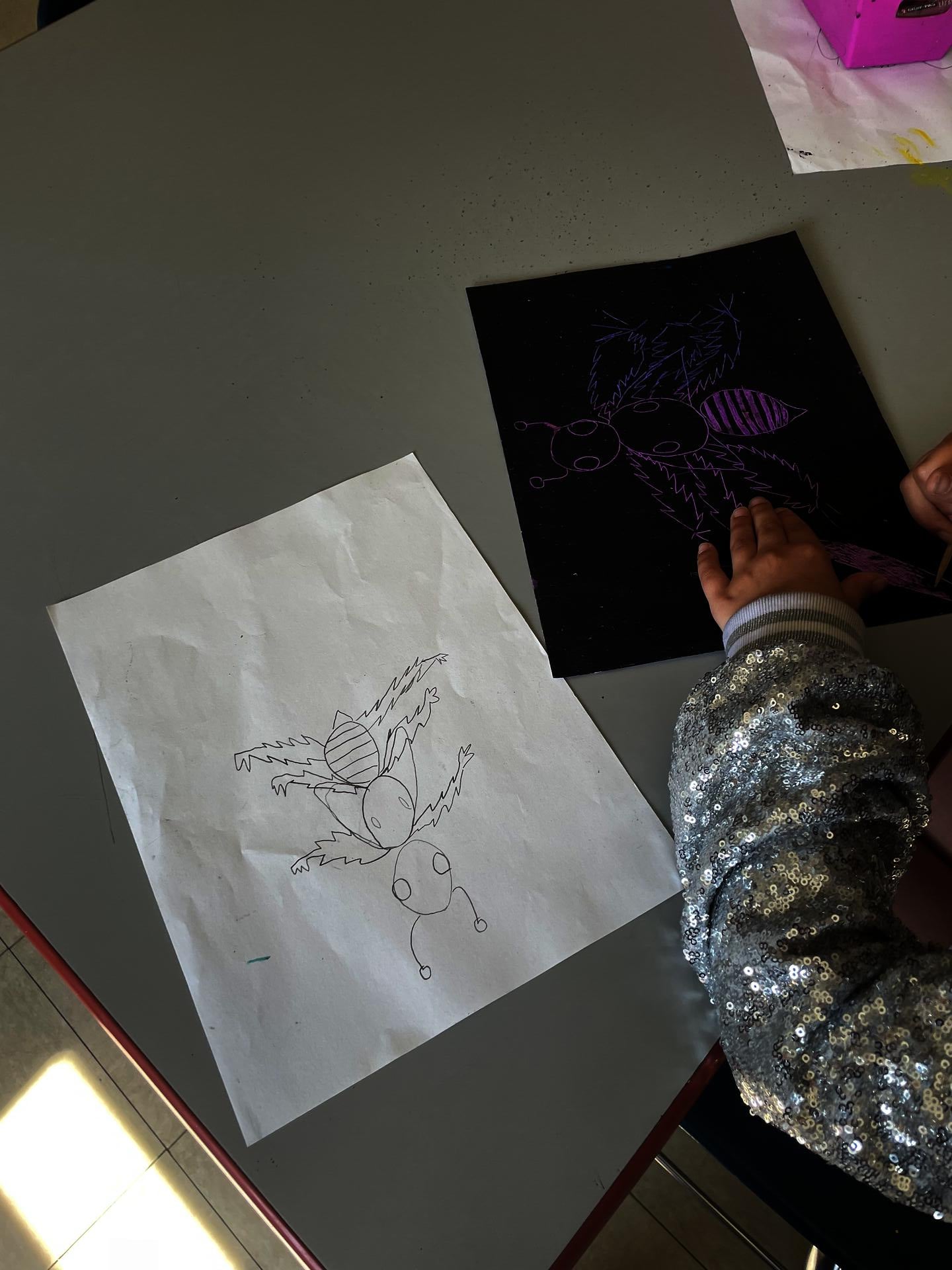 Students use wooden tools to etch into their tempera paint, uncovering color underneath the surface to create an insect with lines. 