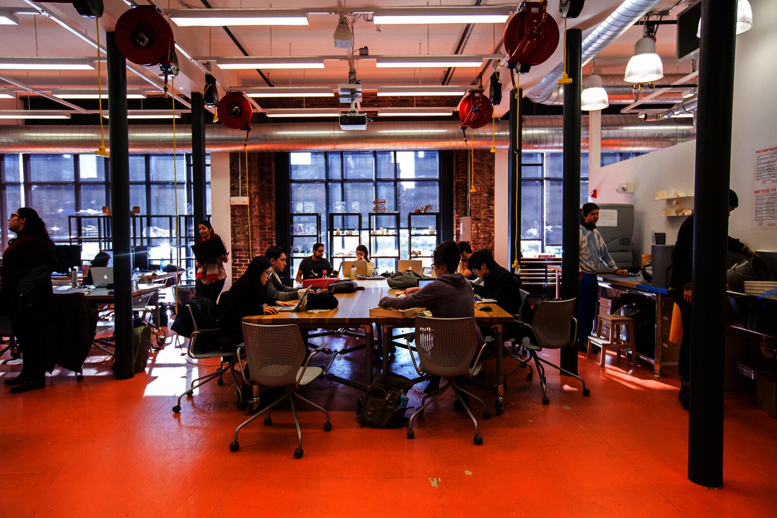 interior shot of co-works, showing students working at large tables in front of floor to ceiling windows. Laser cut and 3D printed objects sit on shelves behind.