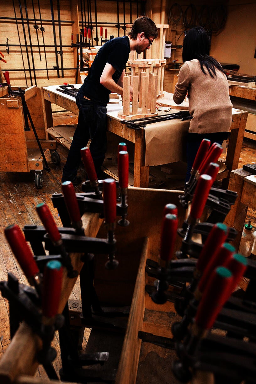 Two people working in a woodshop, with vice clamps in the foreground