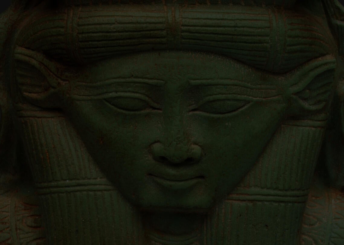 Detail of the jade sculpture’s base, which forms a head with triangular ears, almond shaped eyes, and long eyebrows. Its headdress and hair are textured with rows of etchings.