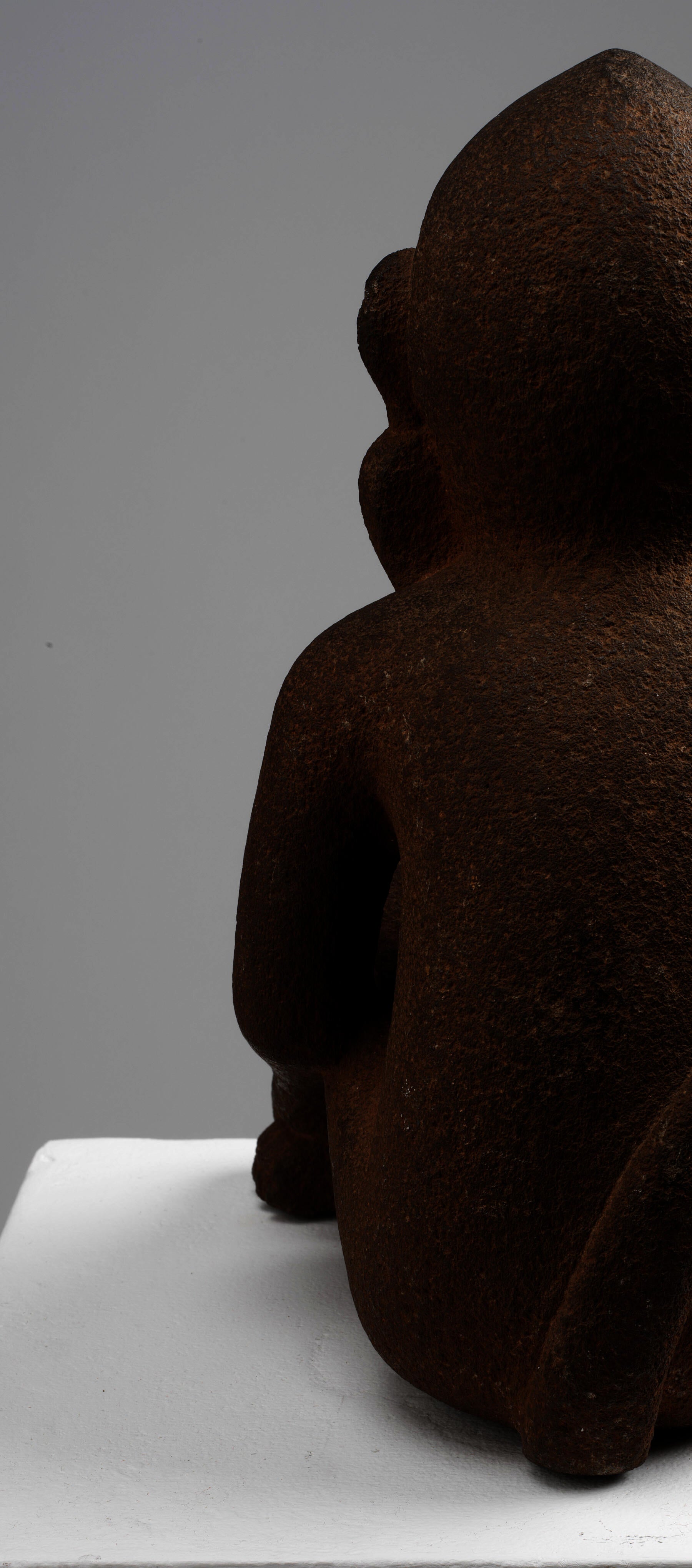 Cutoff back-view of the brown monkey sculpture’s left side. Its earrings are attached to the ear, and its tail goes upwards. The monkey’s texture is rough and porous.