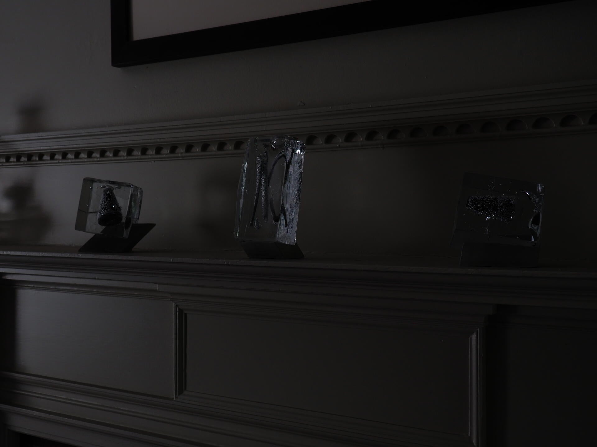 Three glass objects on concrete stands sitting on a fireplace mantle. 