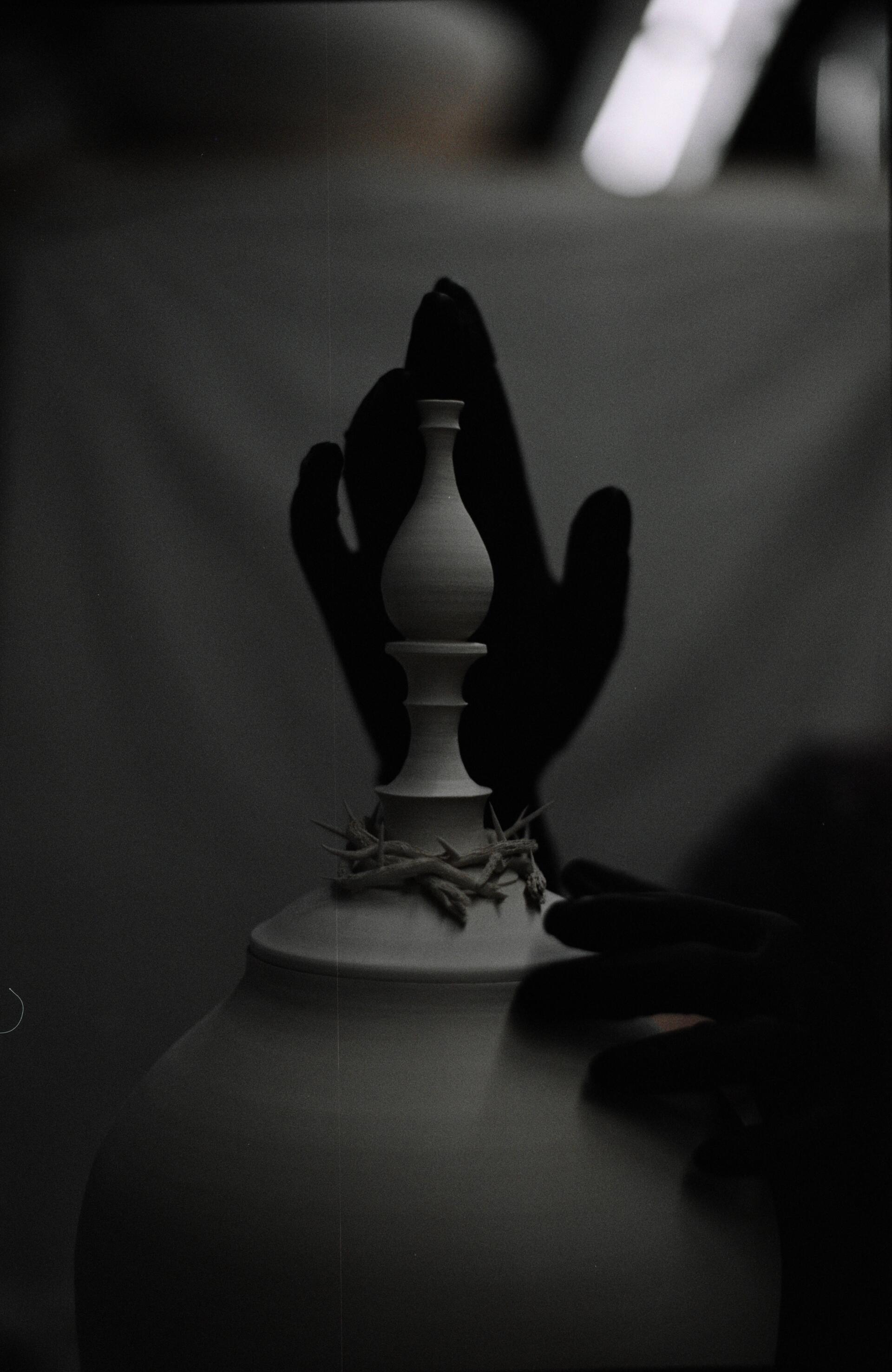 Tall ceramic vase with a hand-sculpted crown of thorns covered in gold luster placed on the neck.