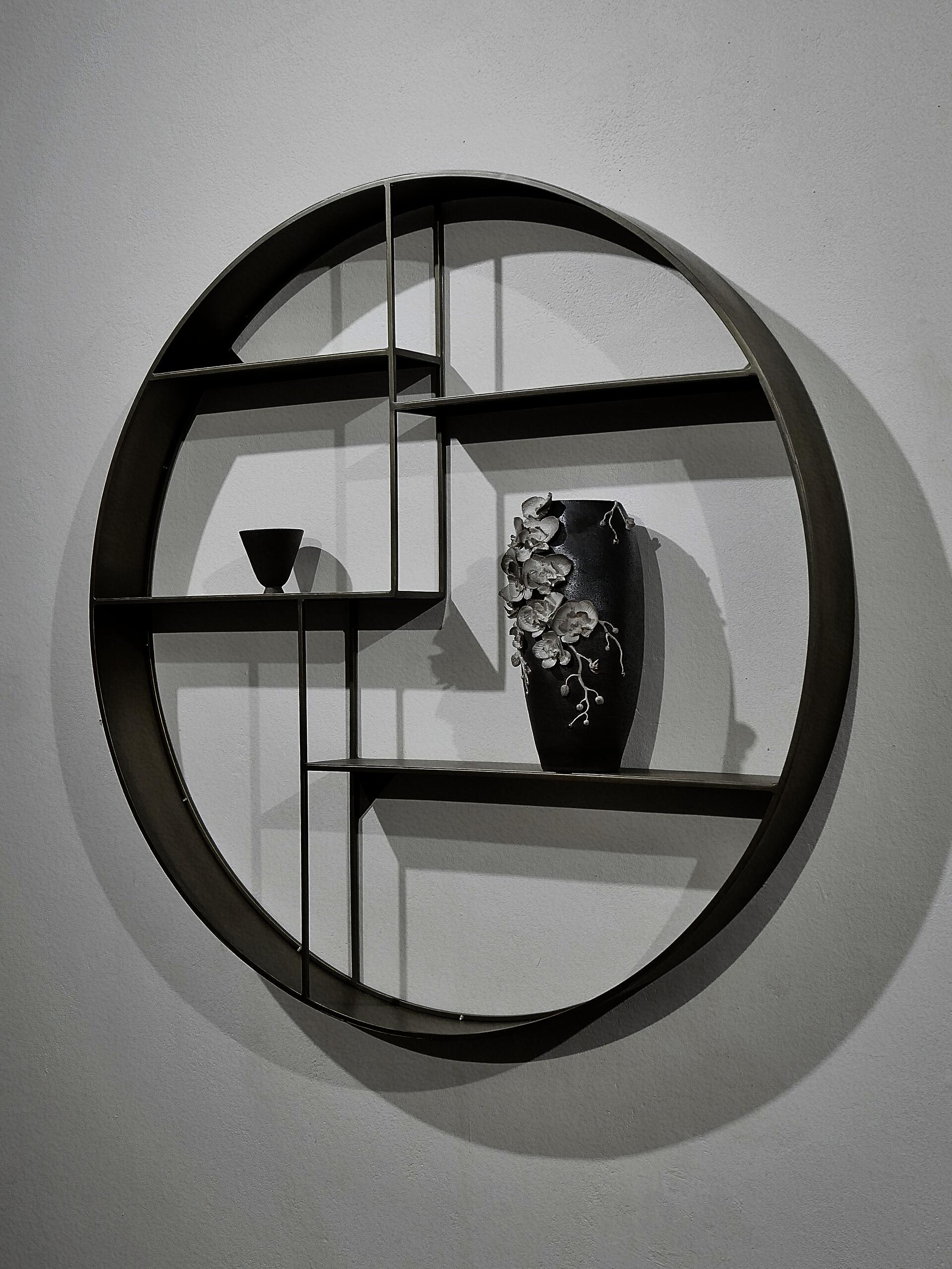 A dark brown Soda-fired ceramic vase with white hand-sculpted orchids and a small tea cup are displayed on a circular wall shelf.