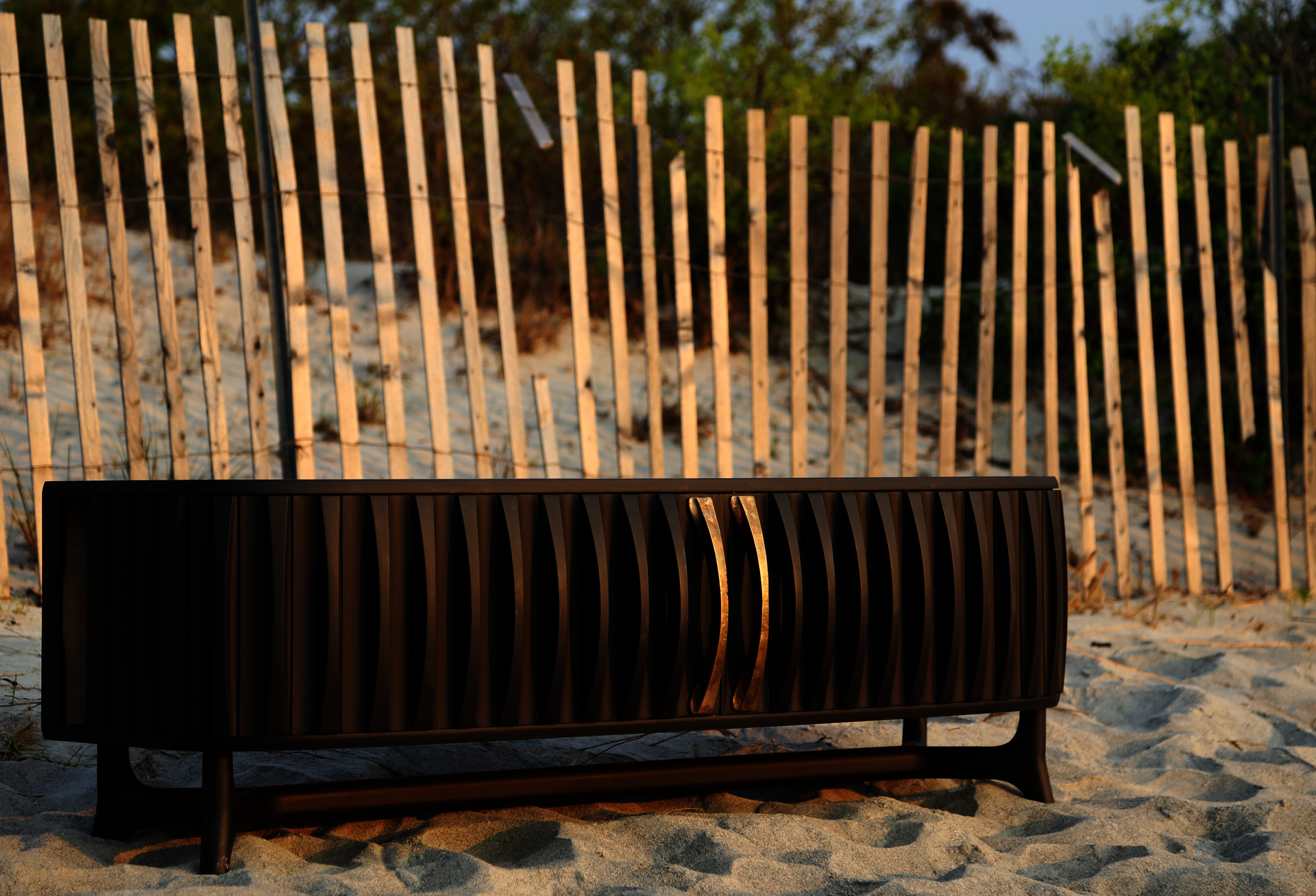 Black media cabinet with bronze handles on beach
