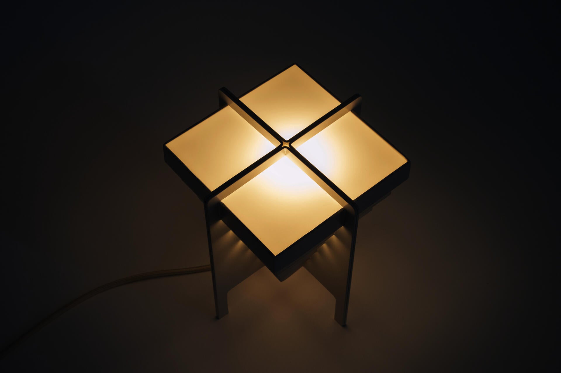 A lamp made of four repeated units and arranged in a way to emphasize the gap between the elements.