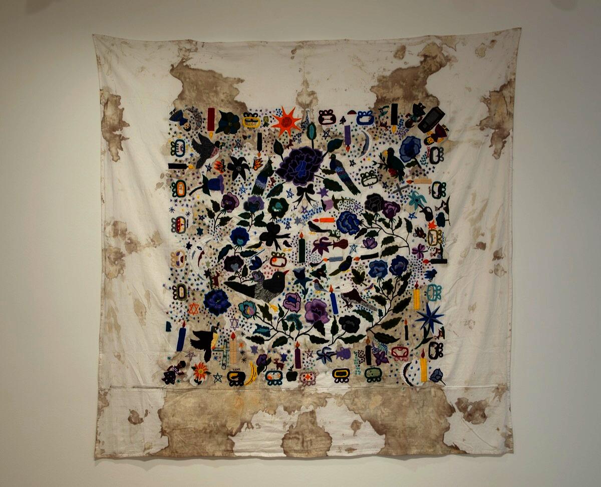 A cloth stained with blood and multiple colorful embroidered flora and fauna atop.