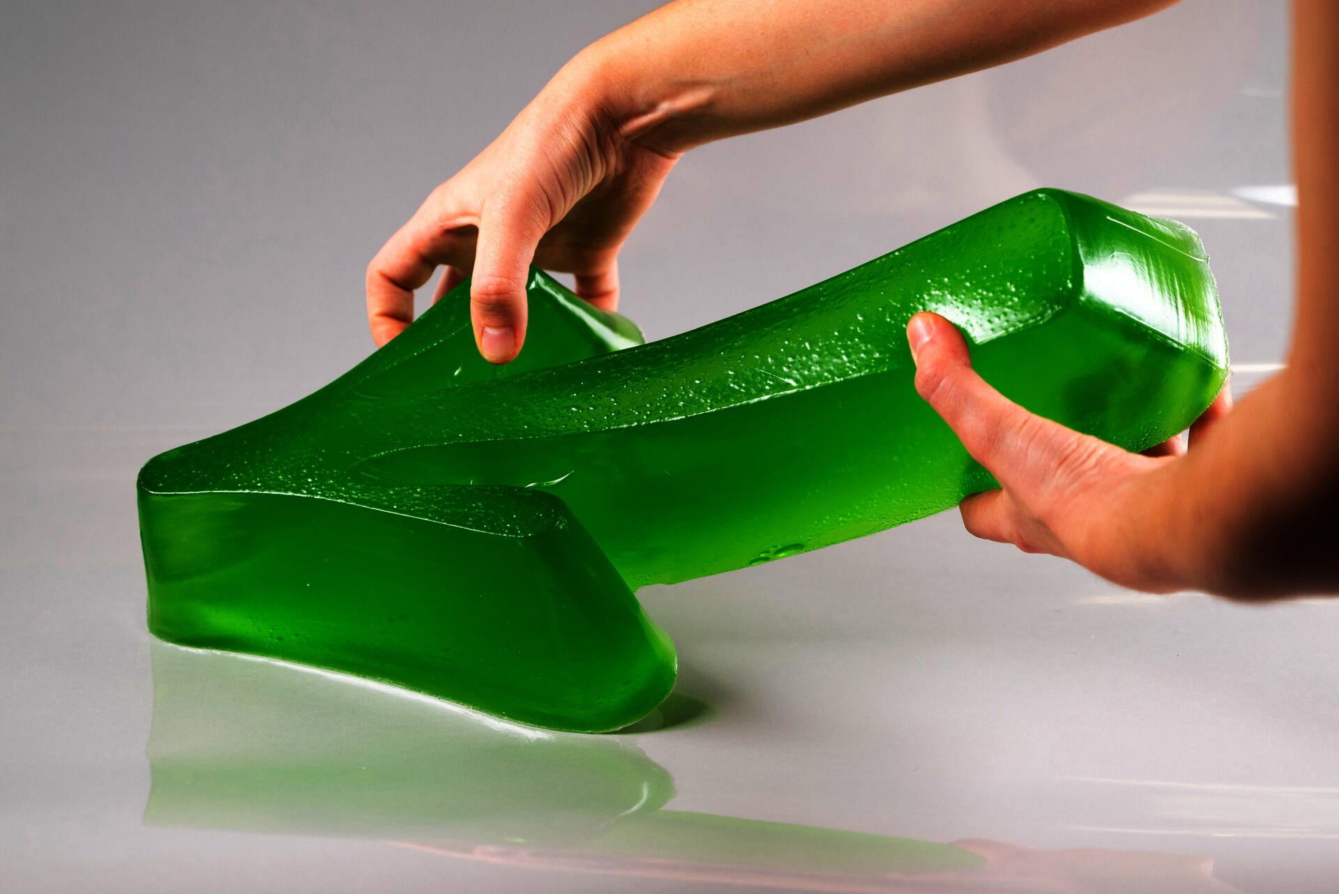 Green gelatin semi-transparent arrow-shaped sculpture, held by two hands.