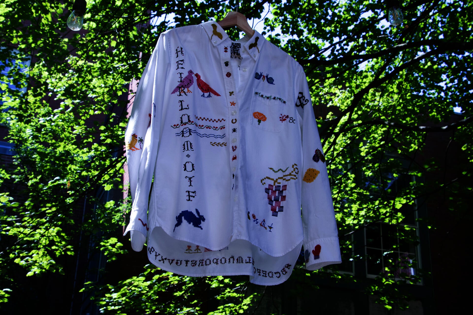 A hanging white-collared shirt that has been embroidered with colorful type and symbols.