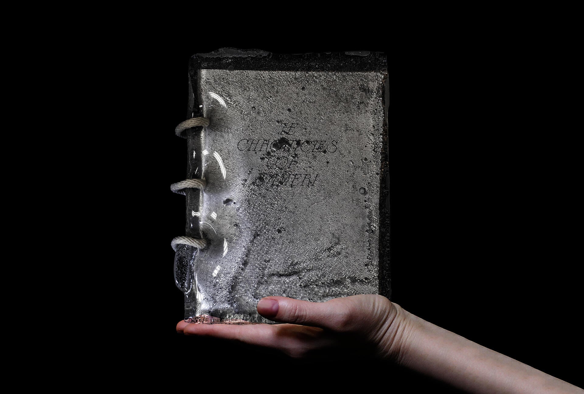 A hand holding a book with thick glass cover and rope binding.