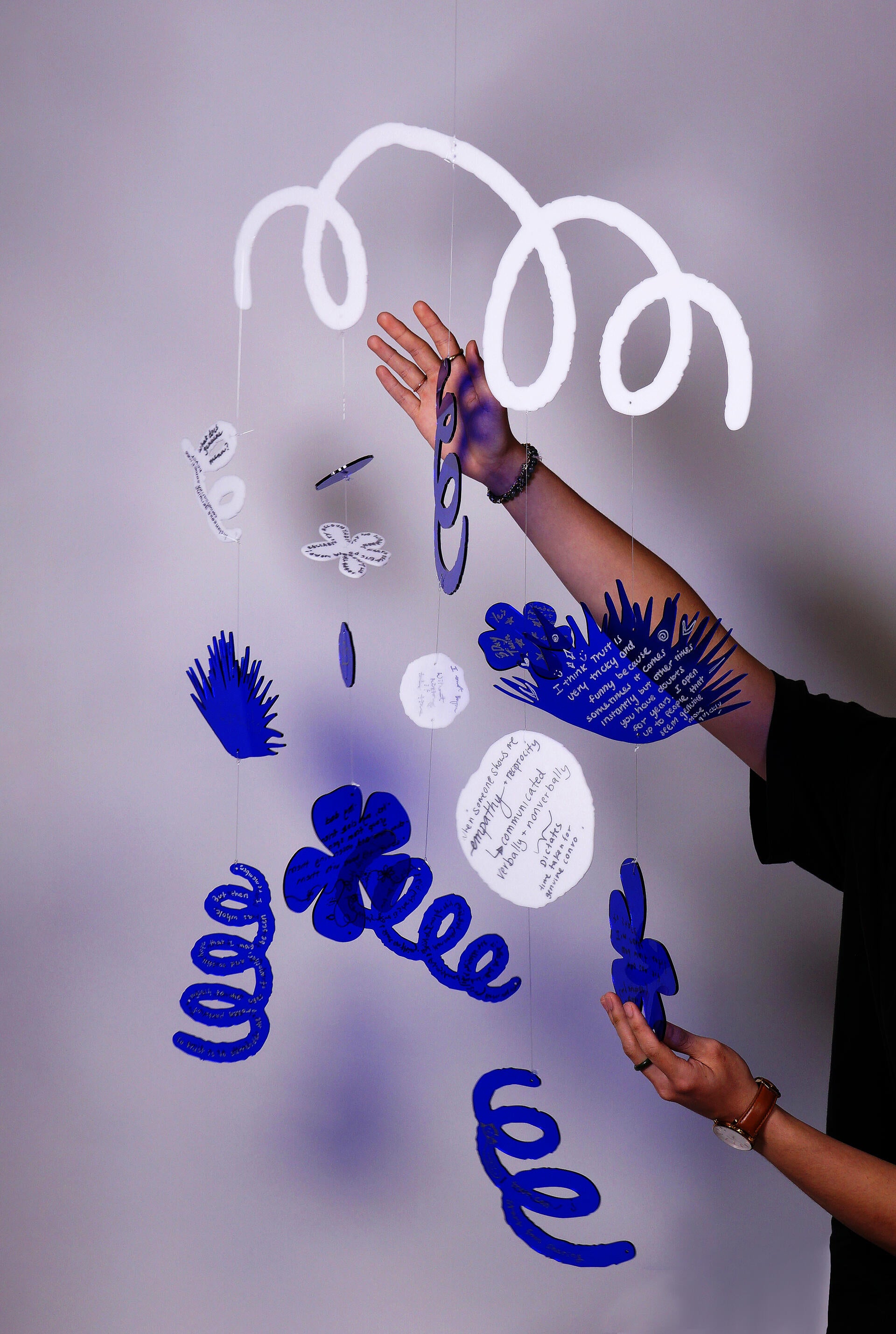 A mobile with transparent blue and white plexiglass cut in shapes of flowers and plants.