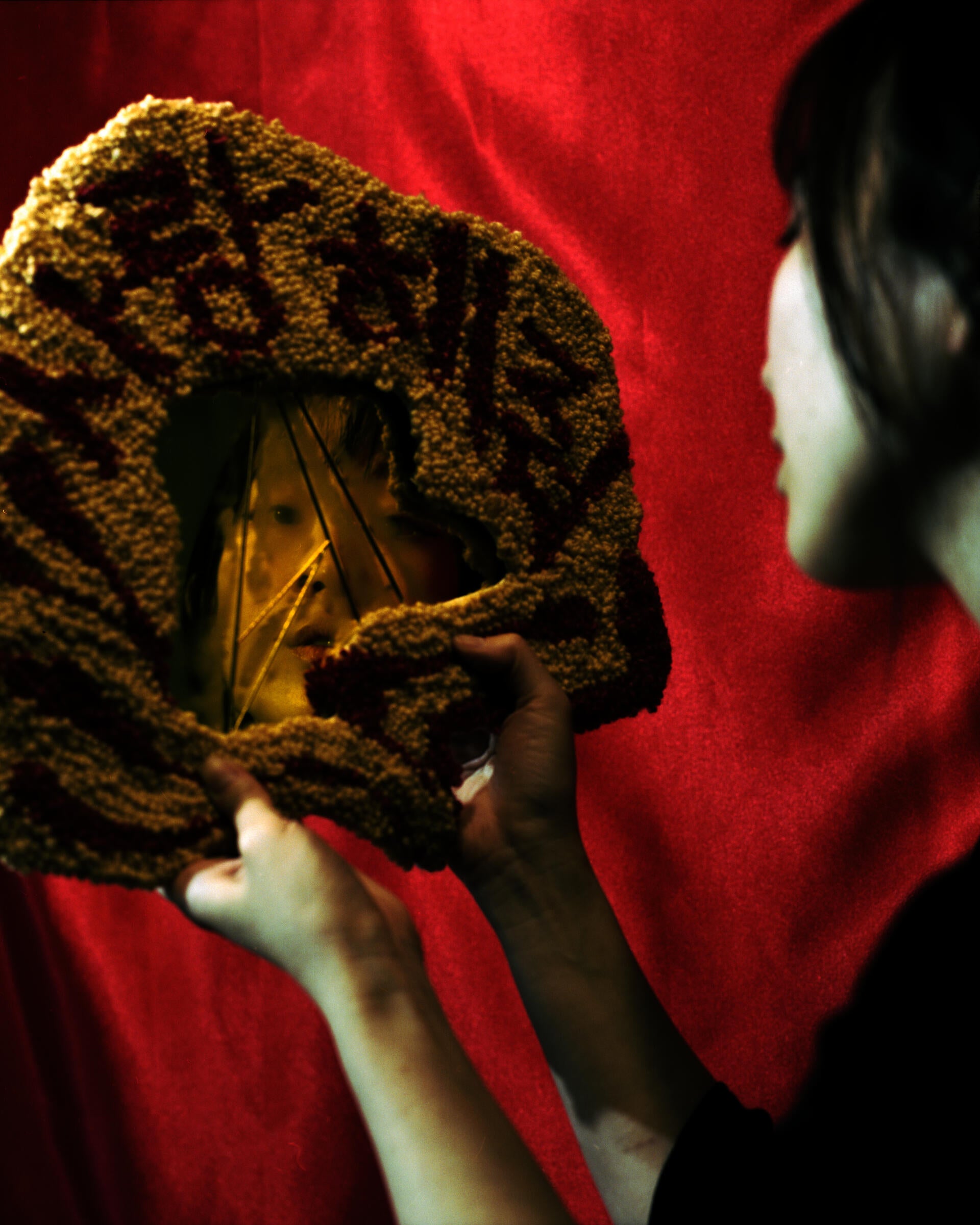 An asian woman looking into a fractured mirror covered with a tufted frame displaying the words "Love Me" in Korean.