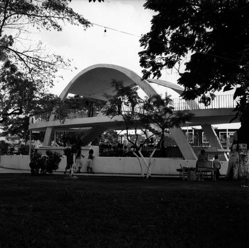 A group of children play underneath an arched, Modernist pavillion.