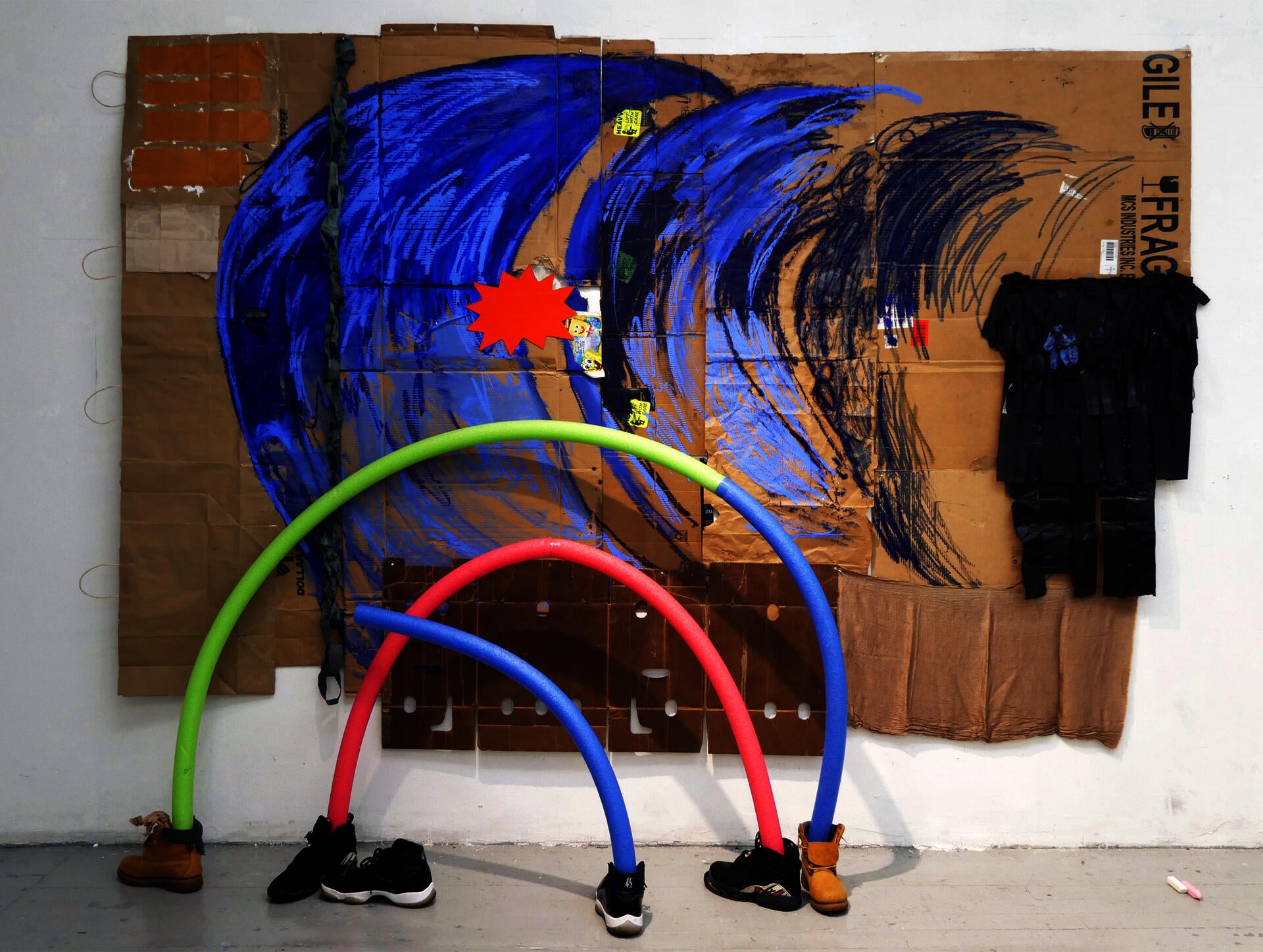 Mixed-media on cardboard and paper bags with foam noodles inside of sneakers.