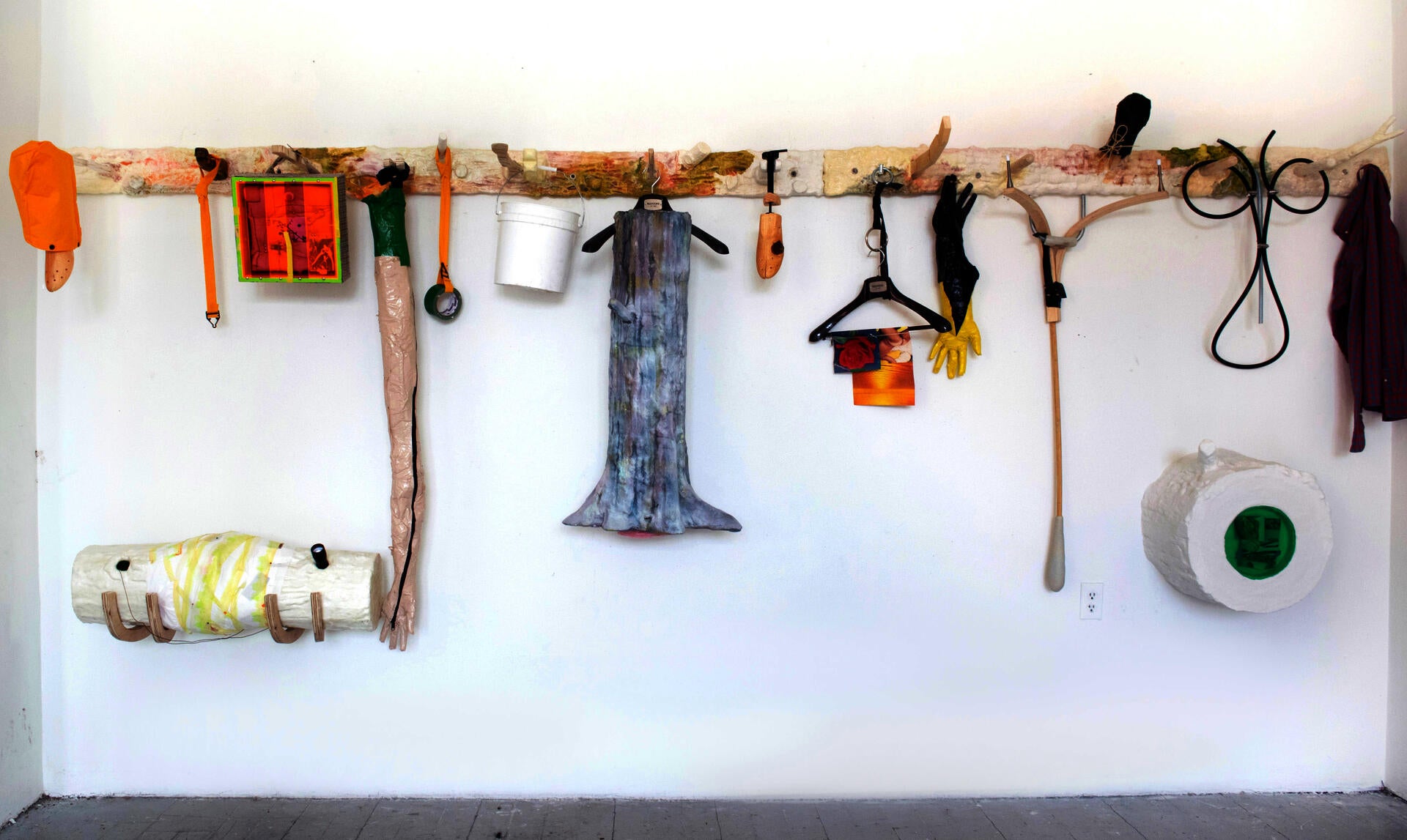 objects of ambiguous function are organized on a pegboard-like sculpture that spans a wall