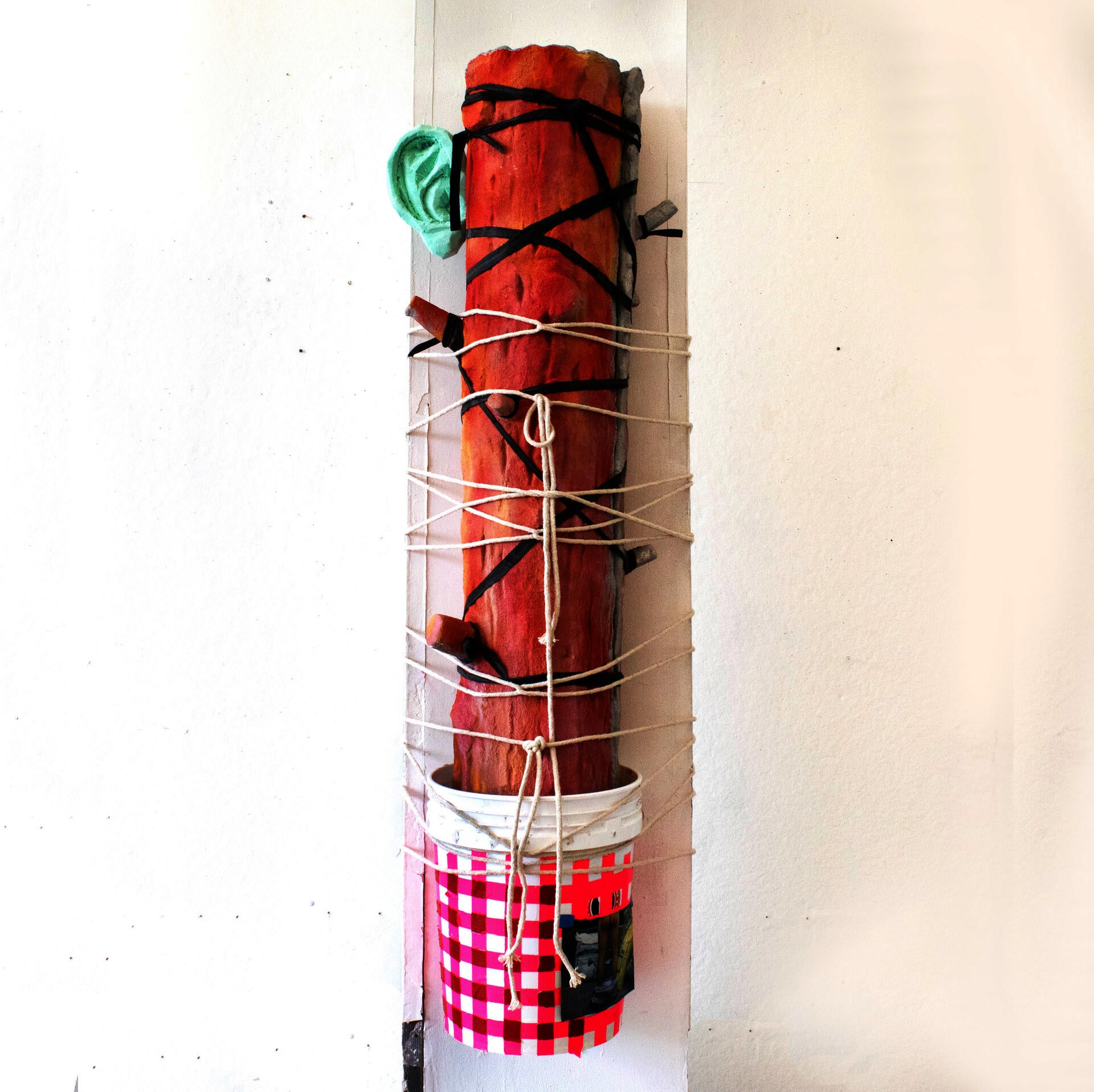 a colorful artificial tree trunk is bound by ropes to a column