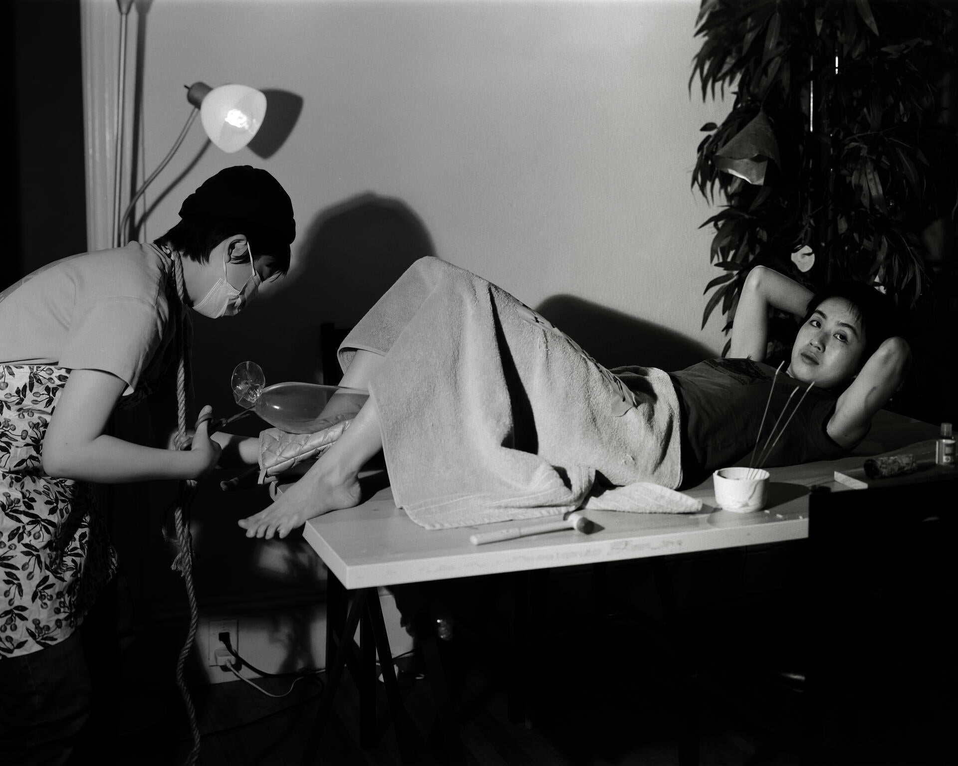 A figure giving birth to a glass object while a doctor-like figure receives it.