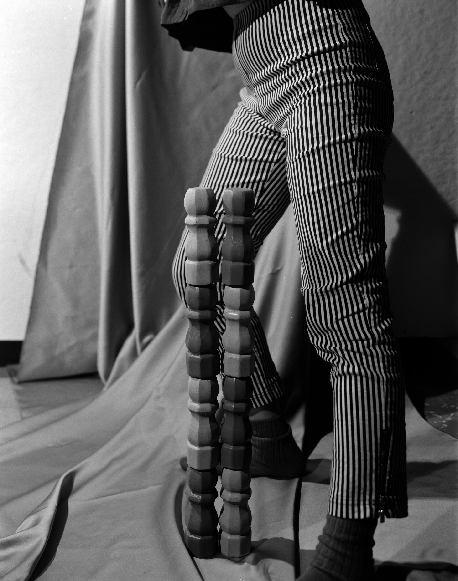 A figure standing in behind a wooden sculpture.