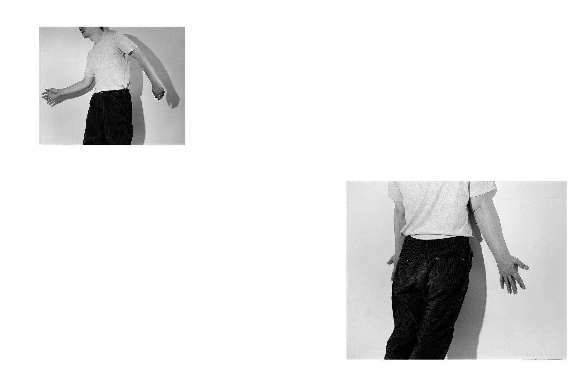 One man striking a peculiar pose while another leans against a wall.