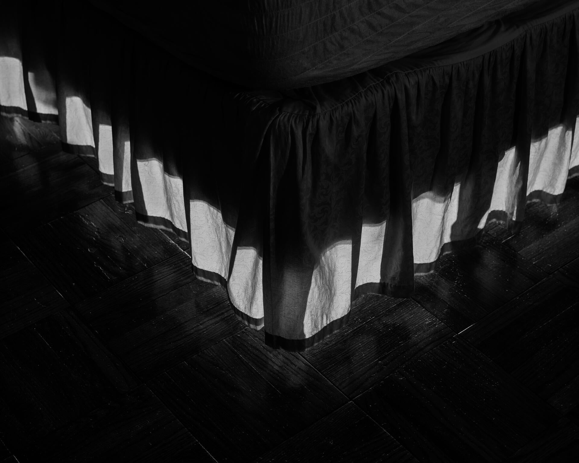Black and white pigment print of bed skirt illuminated from behind.