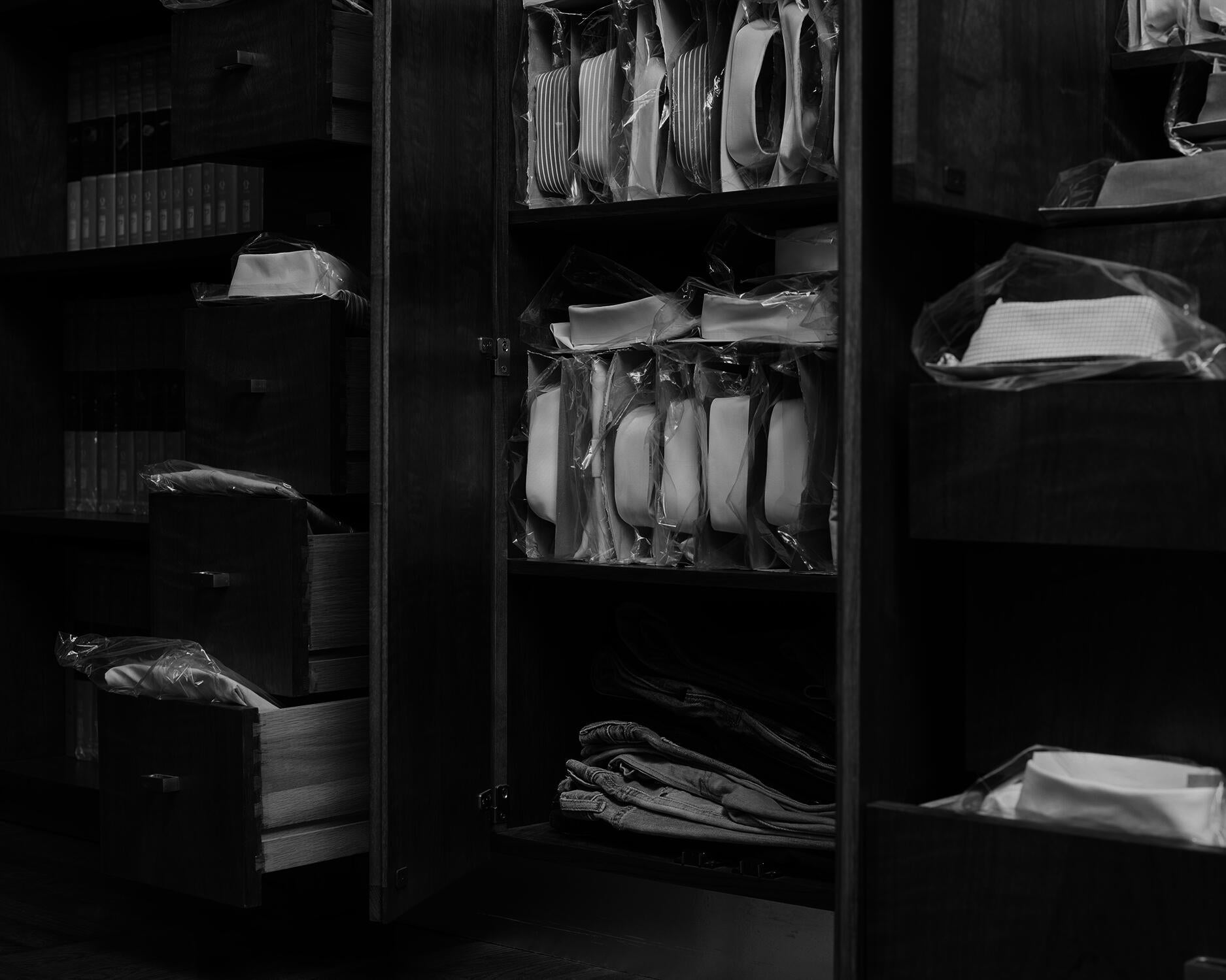 Black and white pigment print of folded shirts emerging from cabinets and drawers.