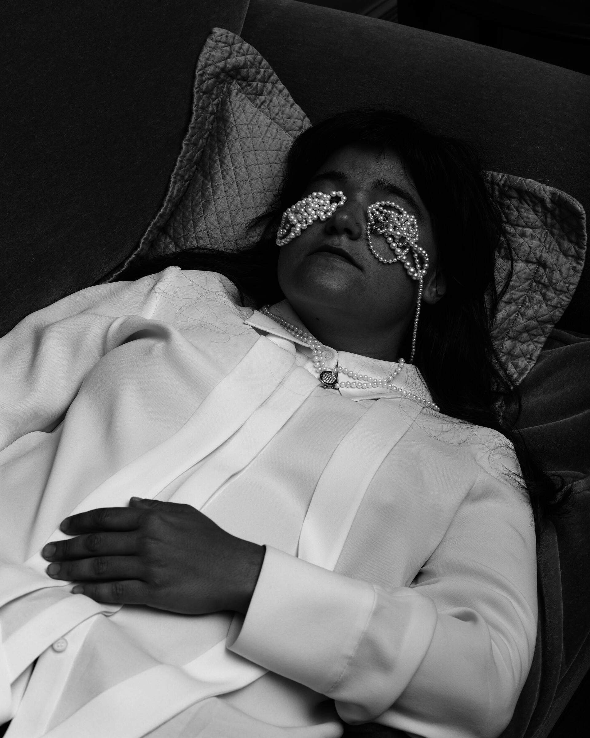 Black and white pigment print of reclining figure wearing strung pearls on their face and neck.