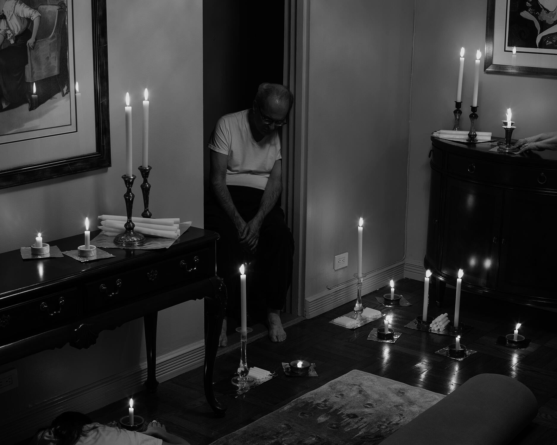 Black and white pigment print of living room with sprawling candle arrangement.