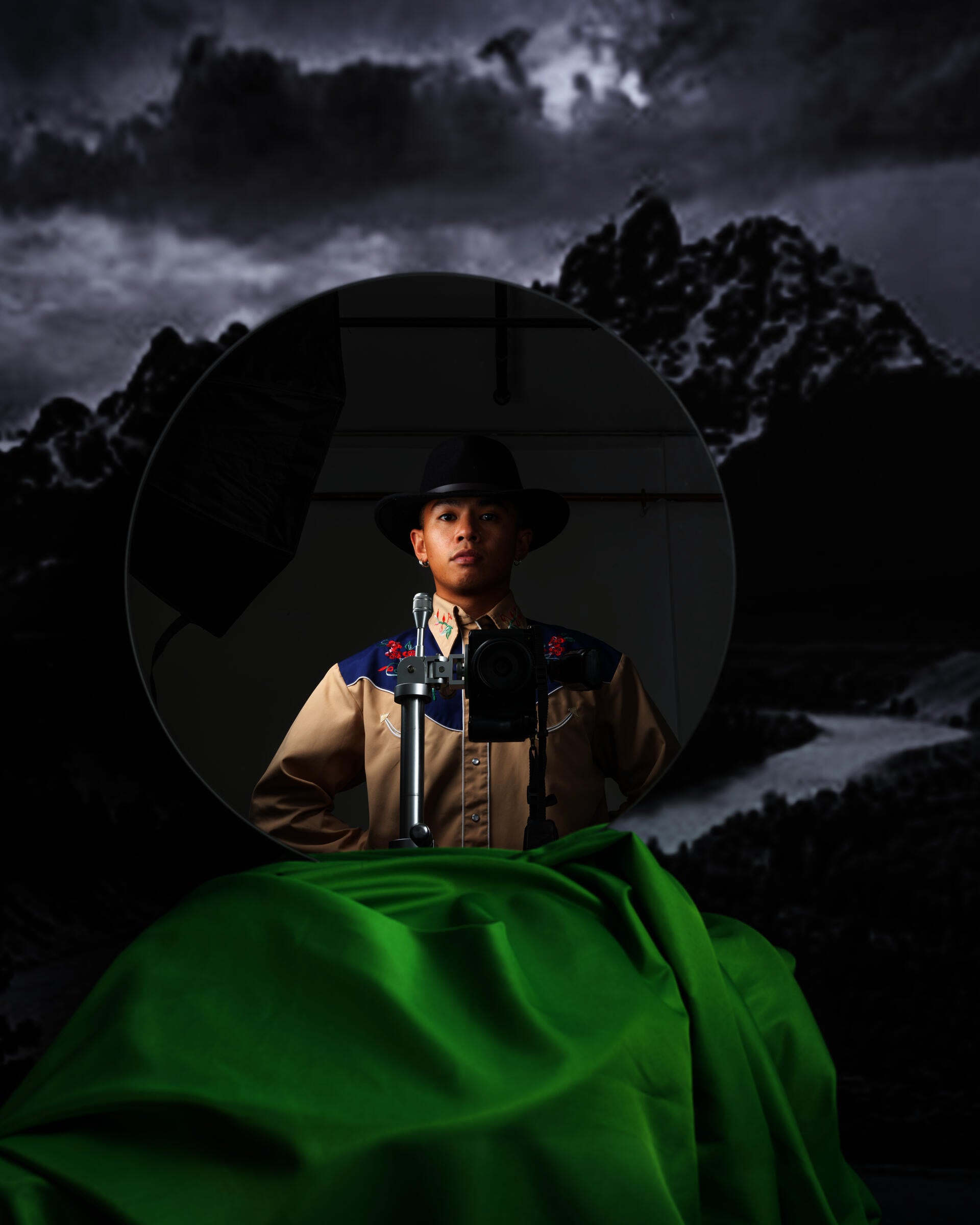A mirror shows a cowboy standing behind a mounted camera. The mirror is propped against a print of an Ansel Adams landscape.