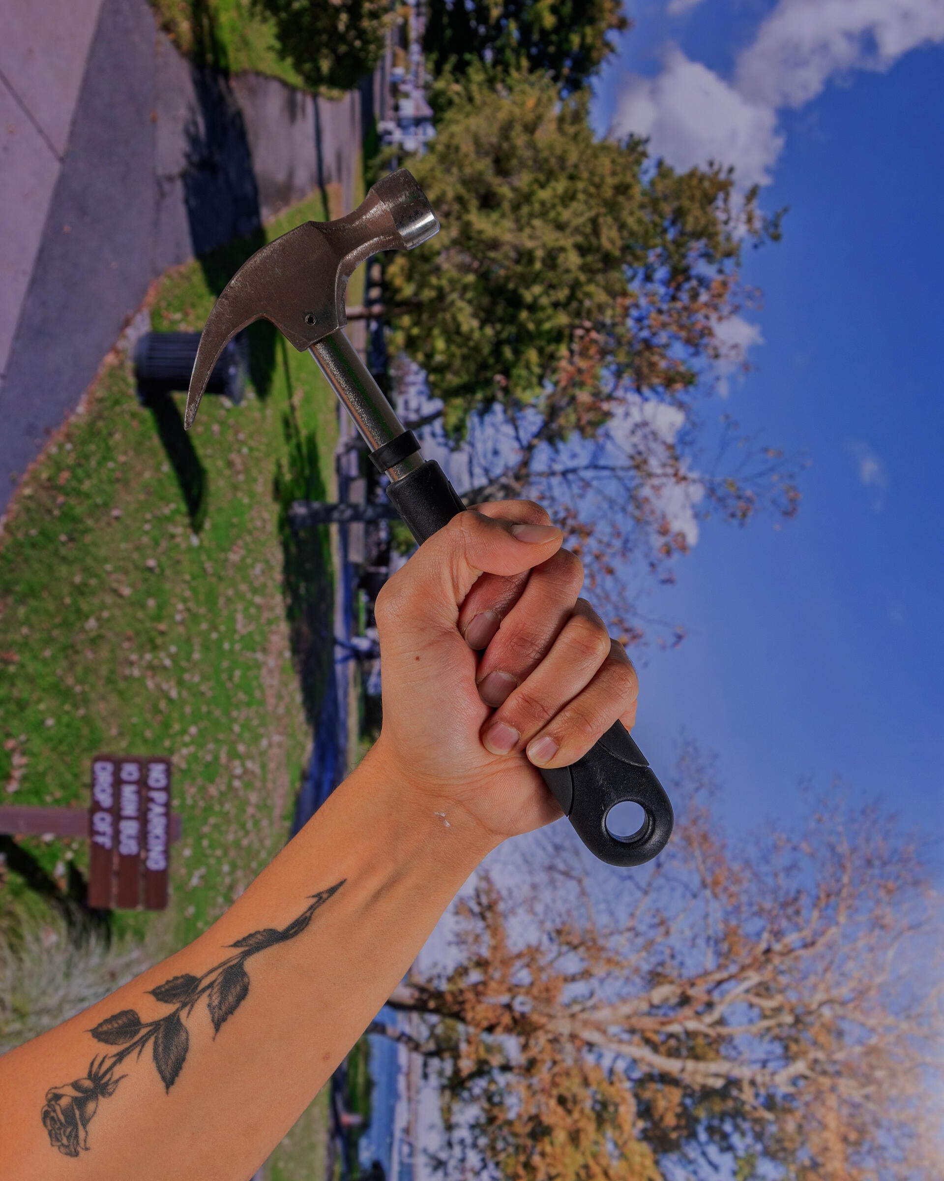 A hand is holding a black and silver hammer, it is against a disoriented backdrop depicting Plymouth, Massachusetts.