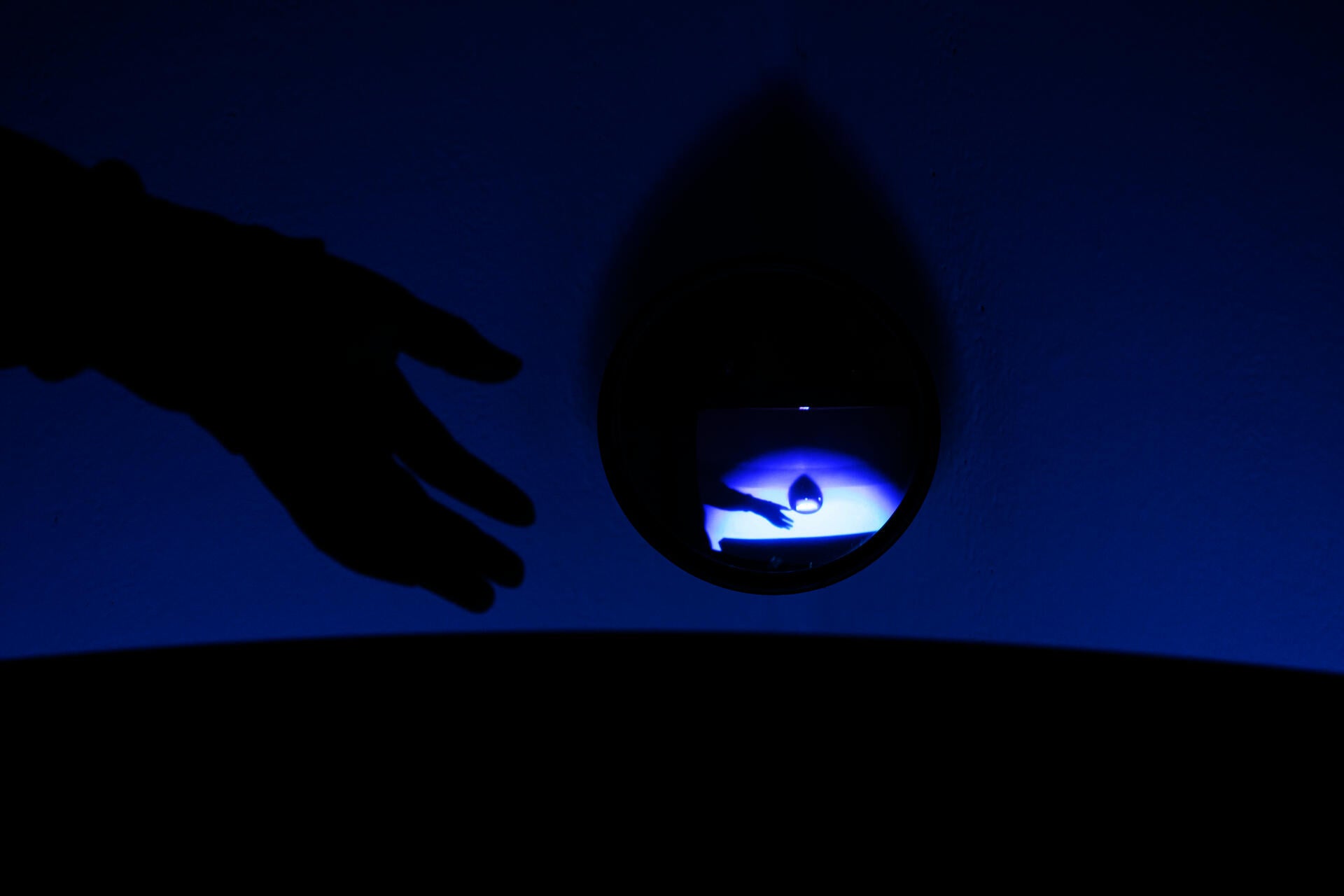 A hand and its reflection in a mirror in colorful light.