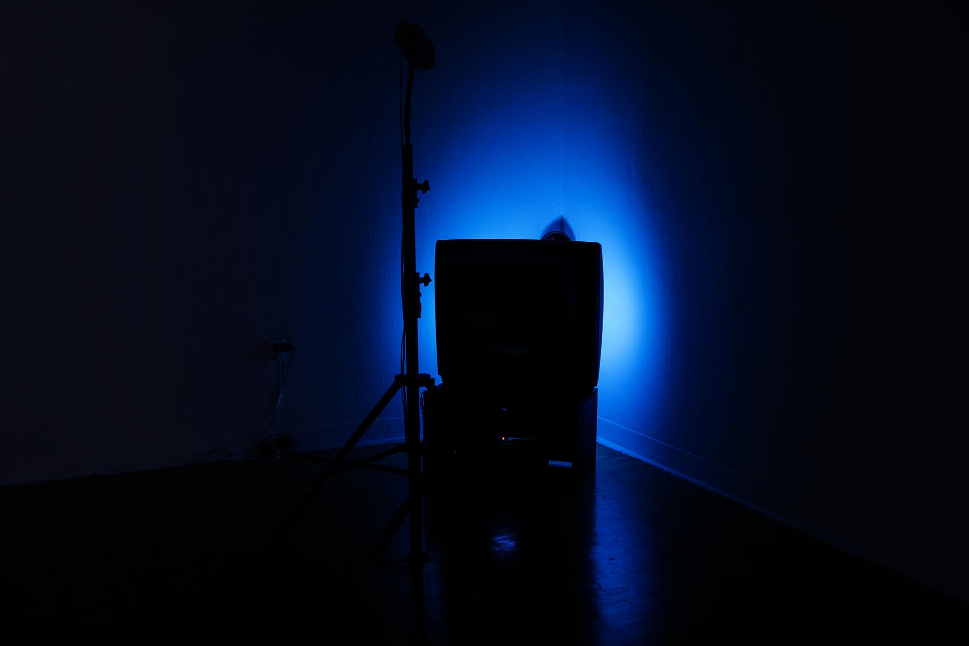 A camera on tripod and a TV placed against a wall corner, reflecting colorful light.