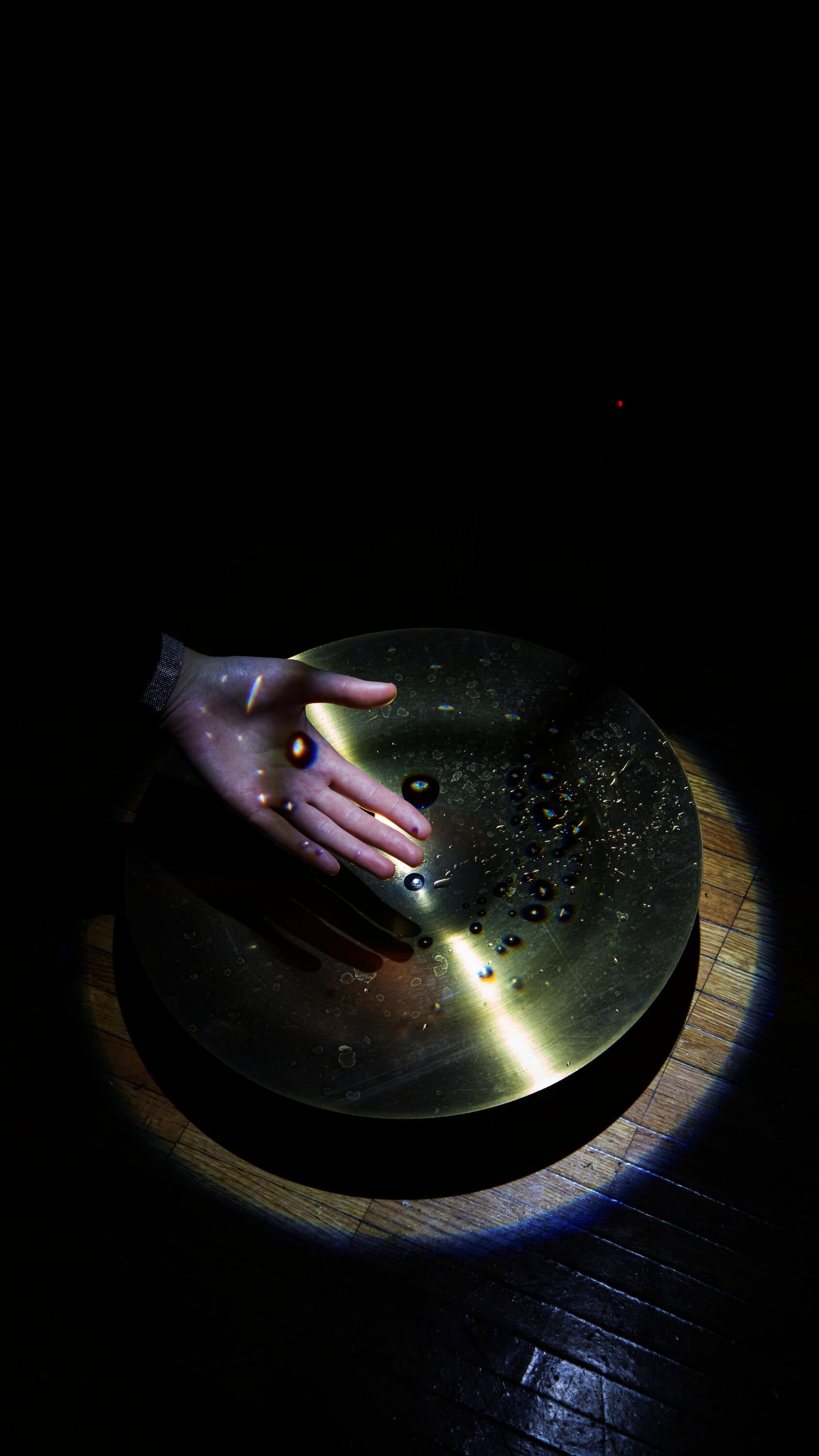 Hand in front of cymbal with water drops projected onto the surface