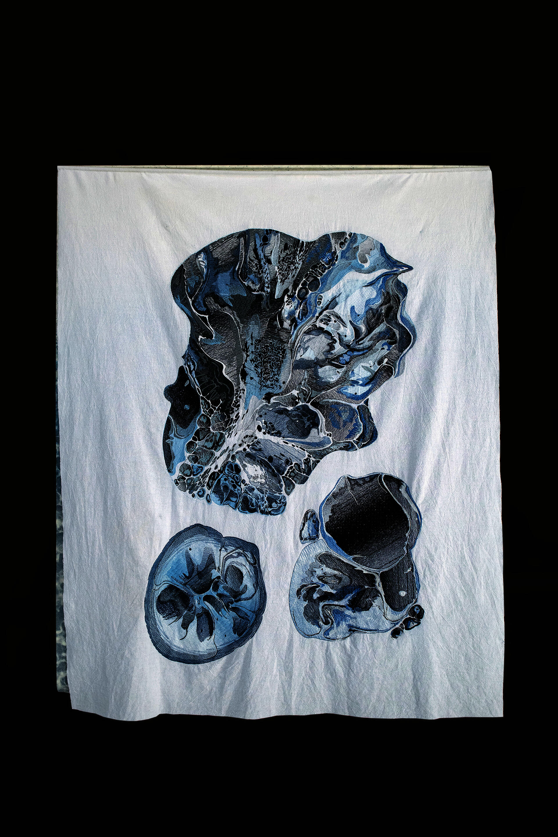 A large piece of white fabric with a frilly texture has three huge oil spots in the shape of intricate blue embroidery.