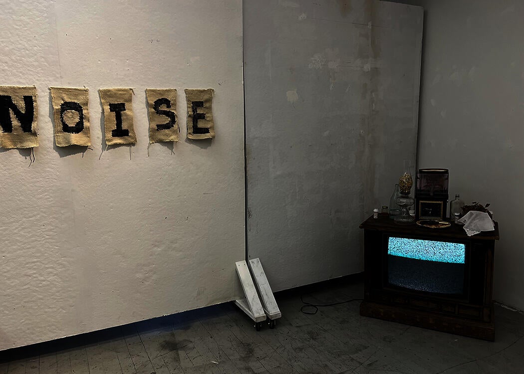 TV with object on top accompanied by a weaving reading "NO WHITE NOISE"