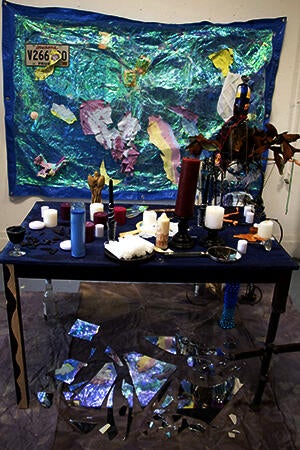 Table with painting and wall piece along with chair sculpture modeled after figure.