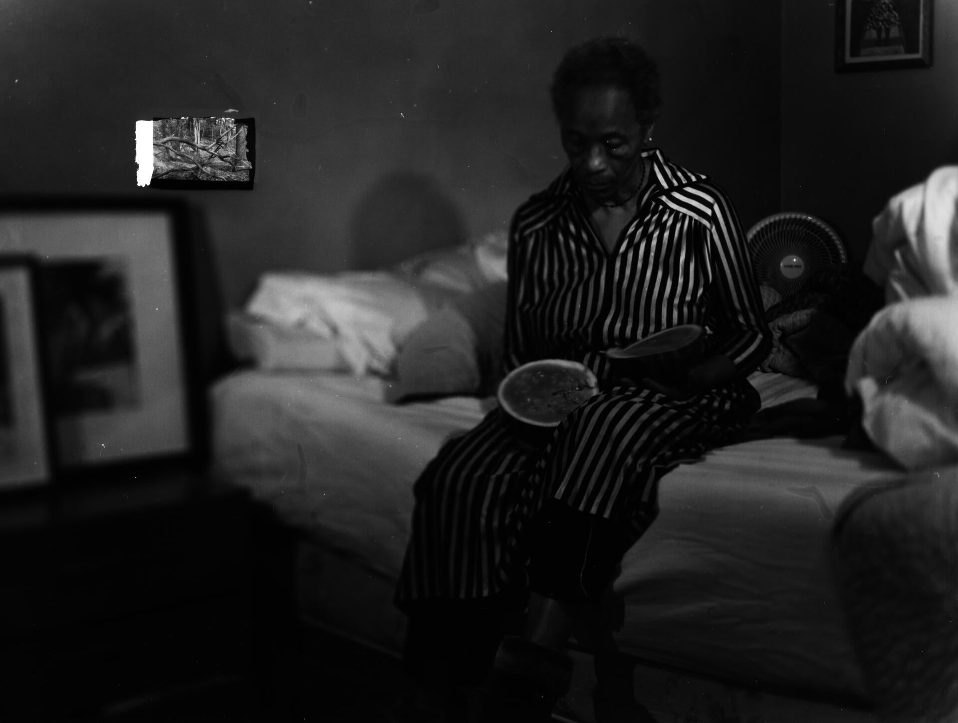 woman sits on bed curiously holding a fruit. in the corner, a glitch appears, a small inlaid image of a forest.