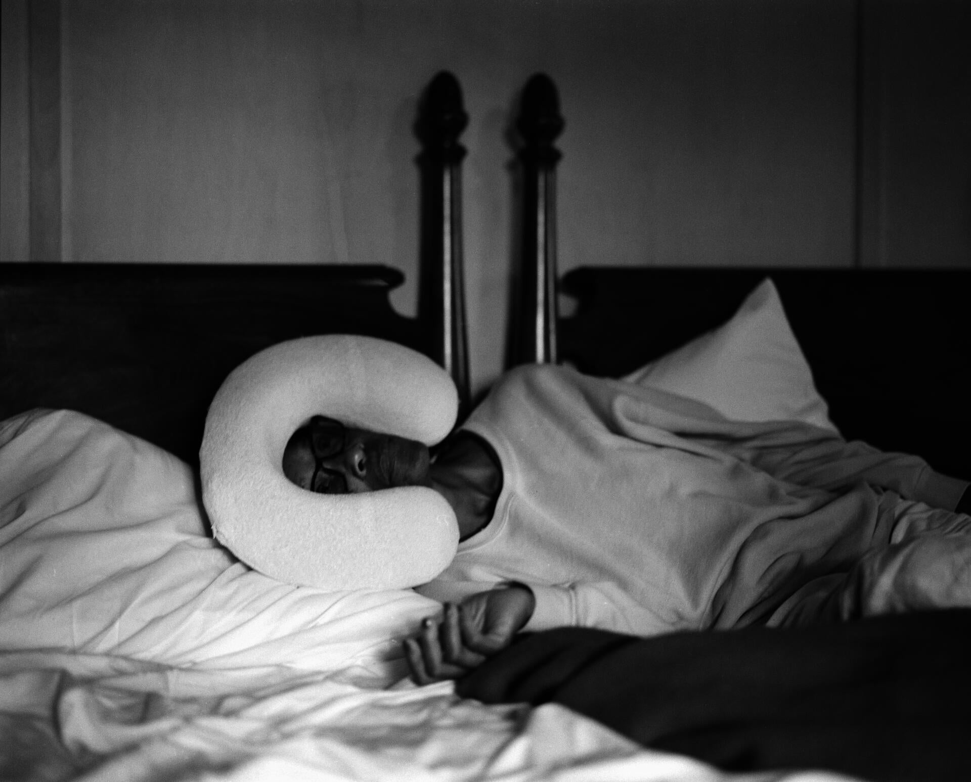 a woman lays on her side on a bed facing the camera, something strange is on her head