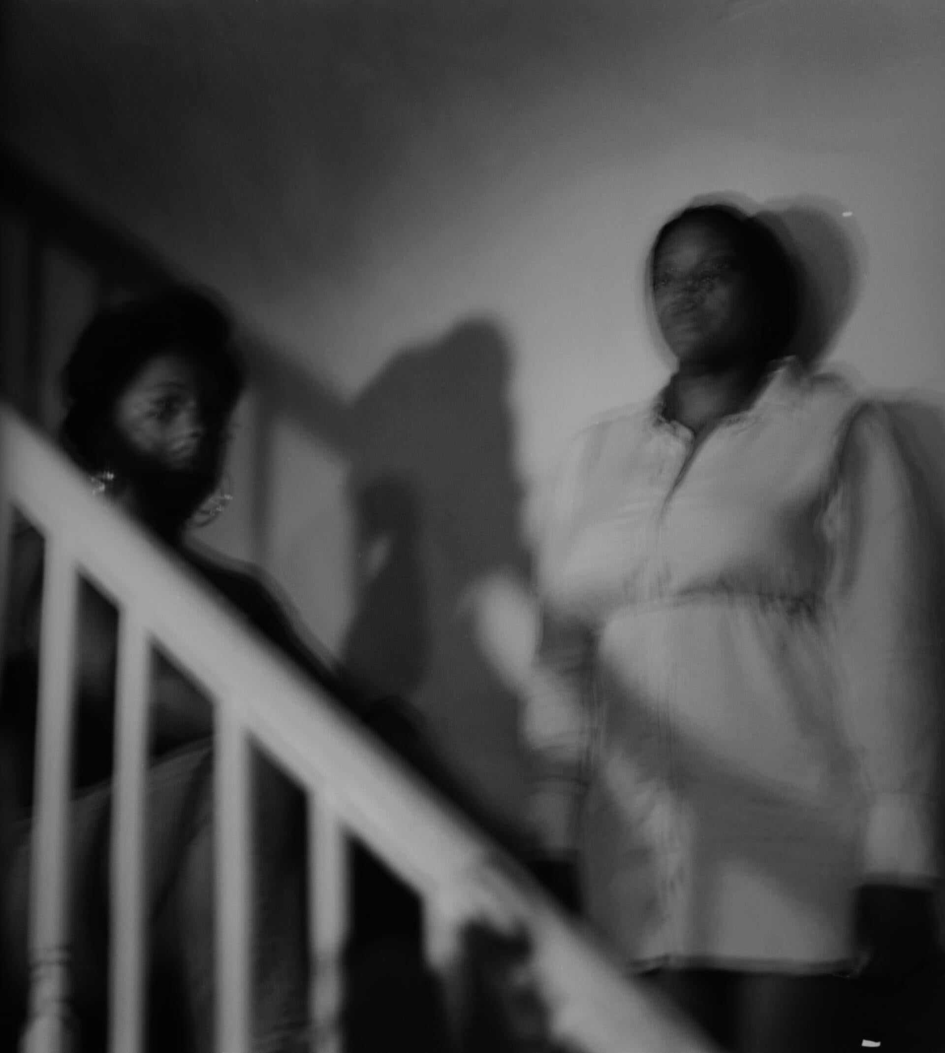two woman, blurred, stand facing the camera on a staircase