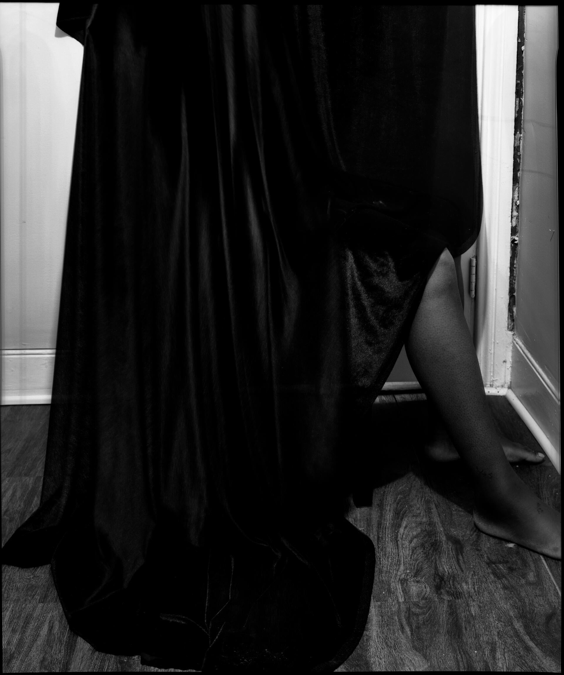 a person sits on a chair, their body covered in a black fabric