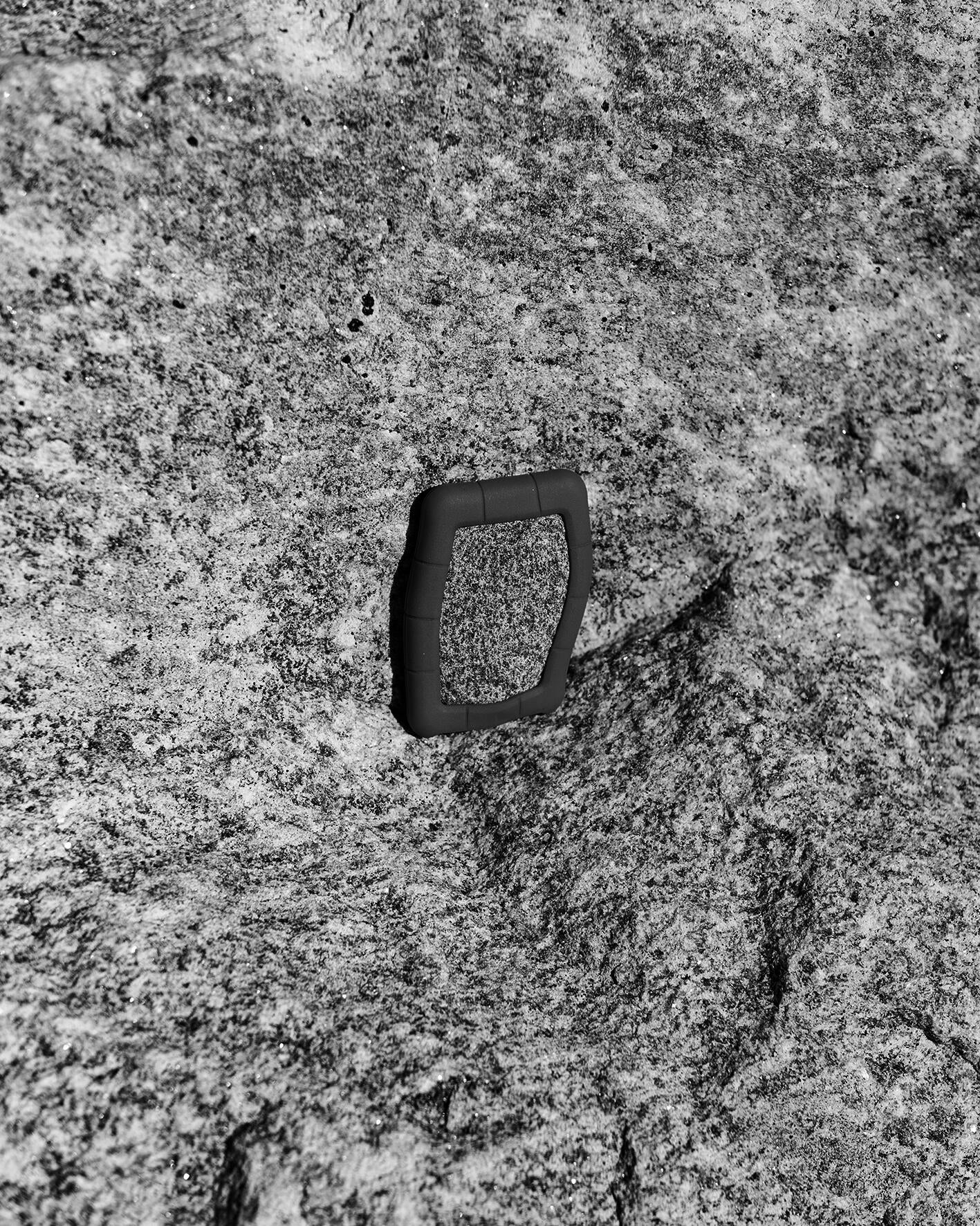 A black and white photo of a granite rock encased in a silicon hard drive cover, positioned against a similar looking granite rock.