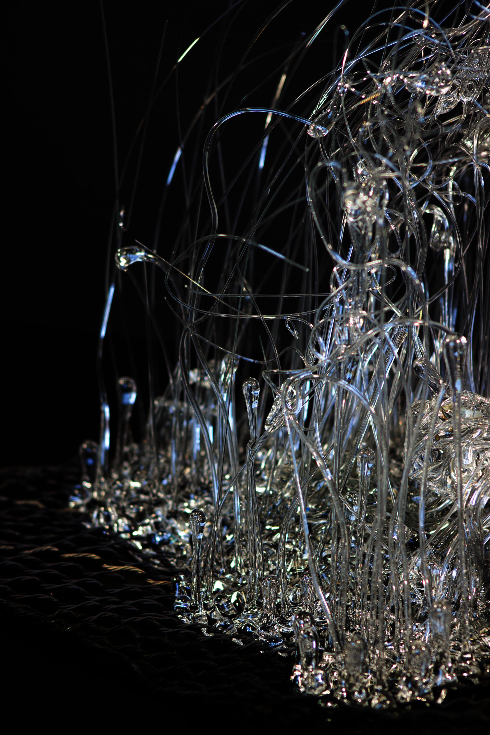 Piece of hand-woven chicken-wire fence with molten glass coming through its holes.