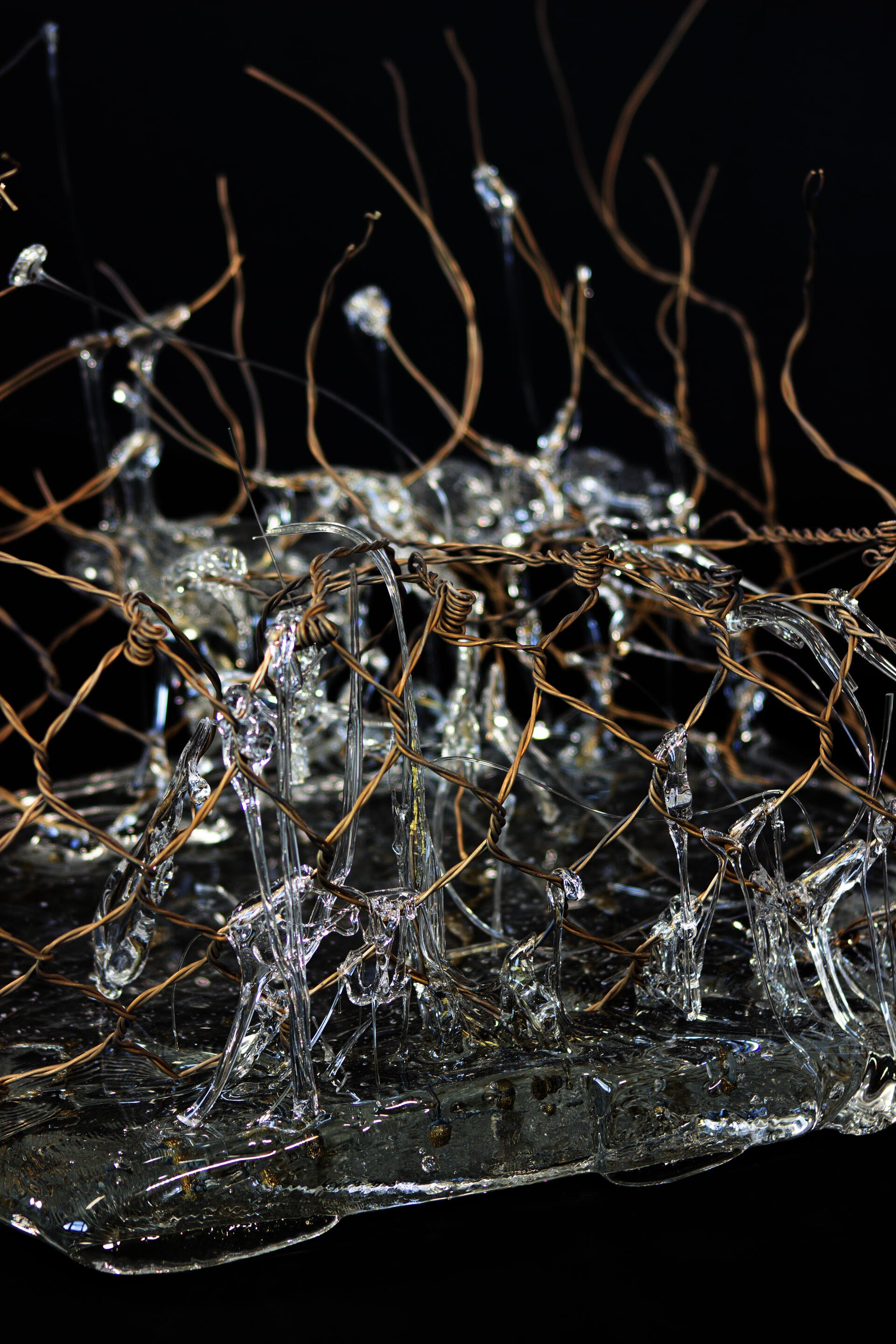 Piece of hand-woven chain-link fence with molten glass encasing some parts of it.
