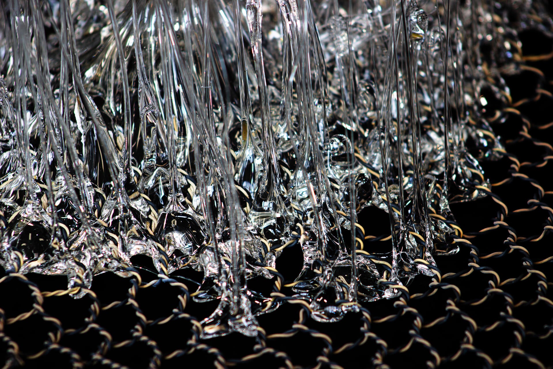 Piece of a hand-woven chicken-wire fence with molten glass coming through its holes.