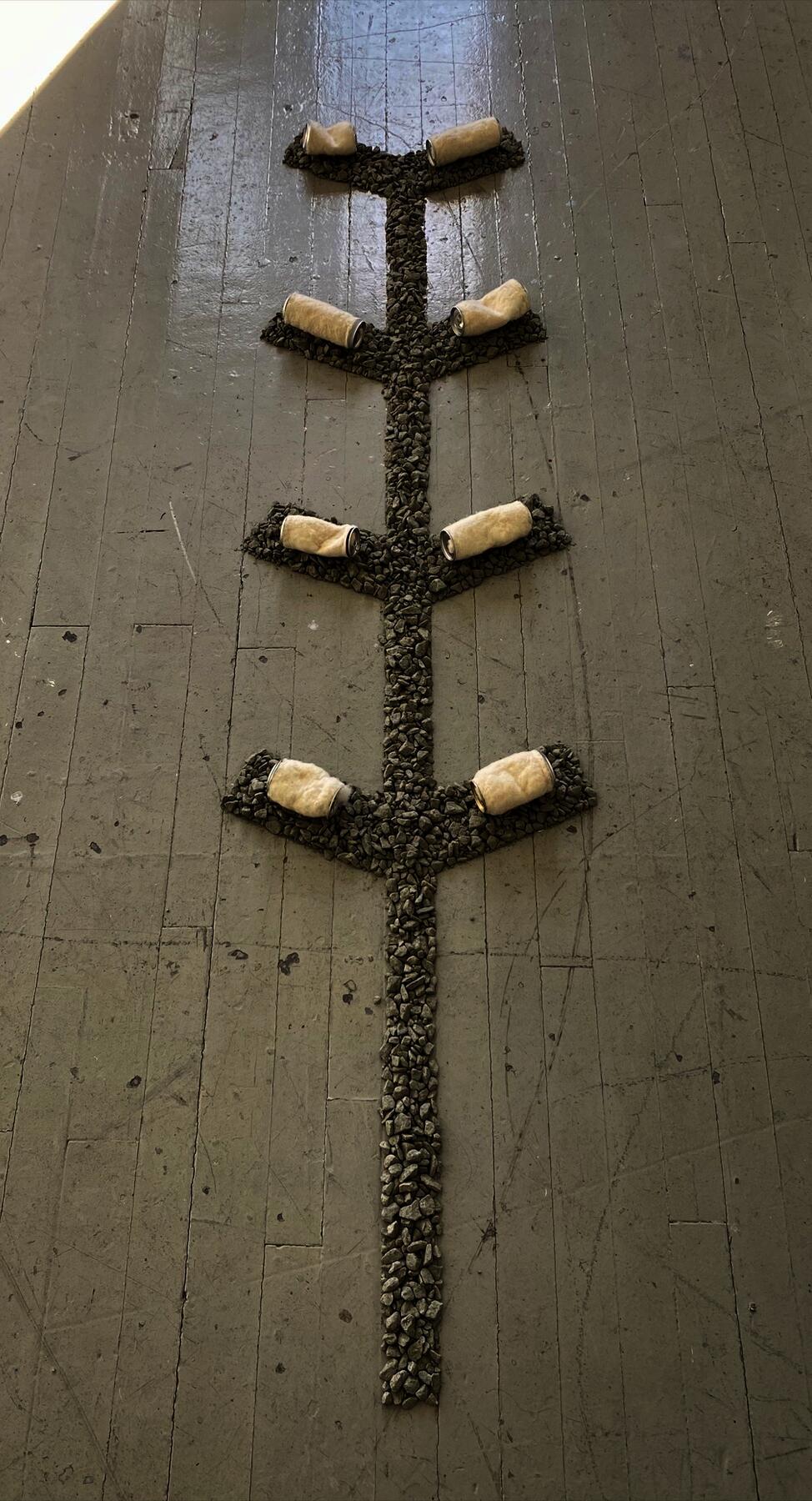 Loose gravel forms a shape on the floor, with felted aluminum cans placed on top.
