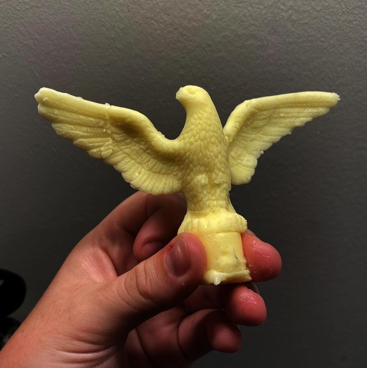 A white person's hand holds a miniature American eagle made of butter.