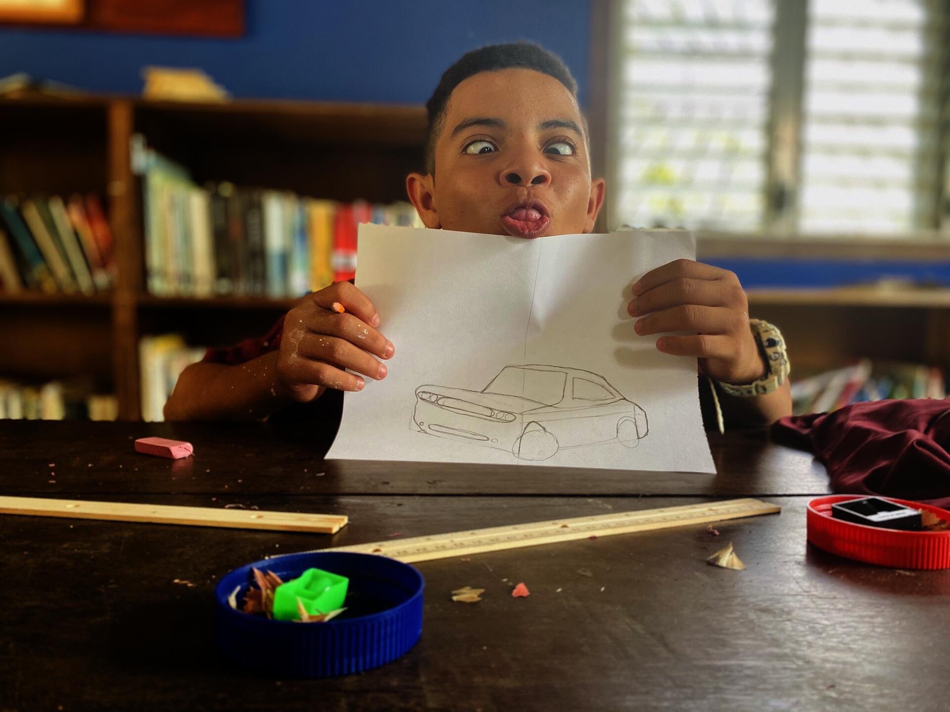 Middle school student holding pencil drawing of a car and making a silly face.