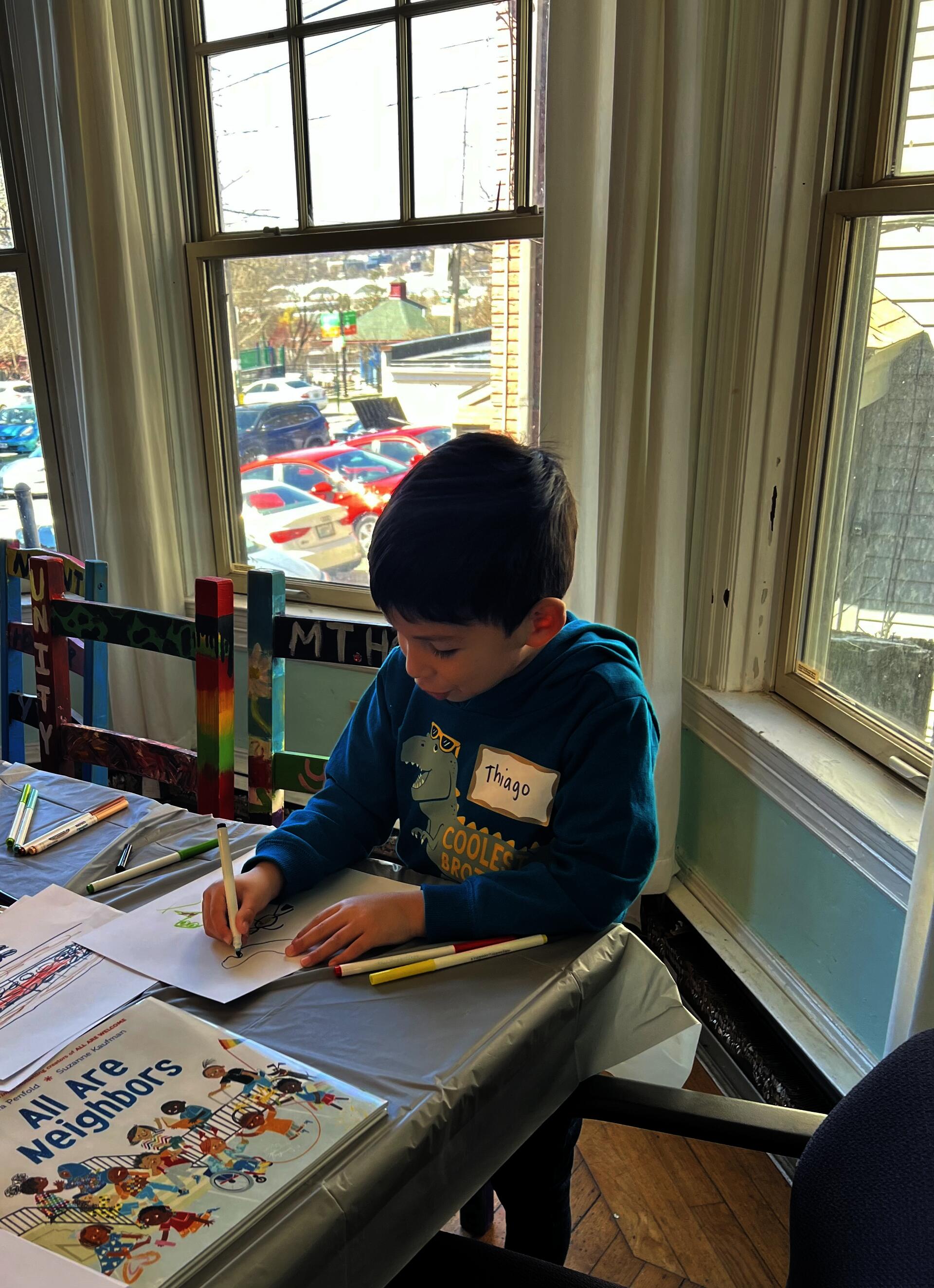 Student sitting at a table and drawing with marker.