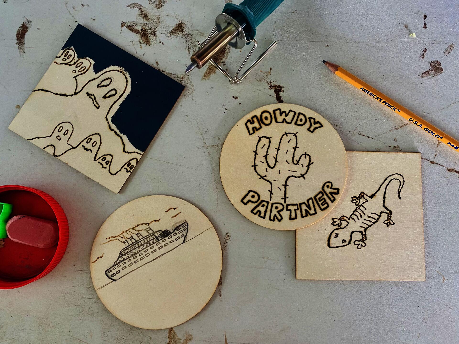 Two wooden squares and two wooden circles with burned images of a lizard, a ship, a cactus, and ghosts.