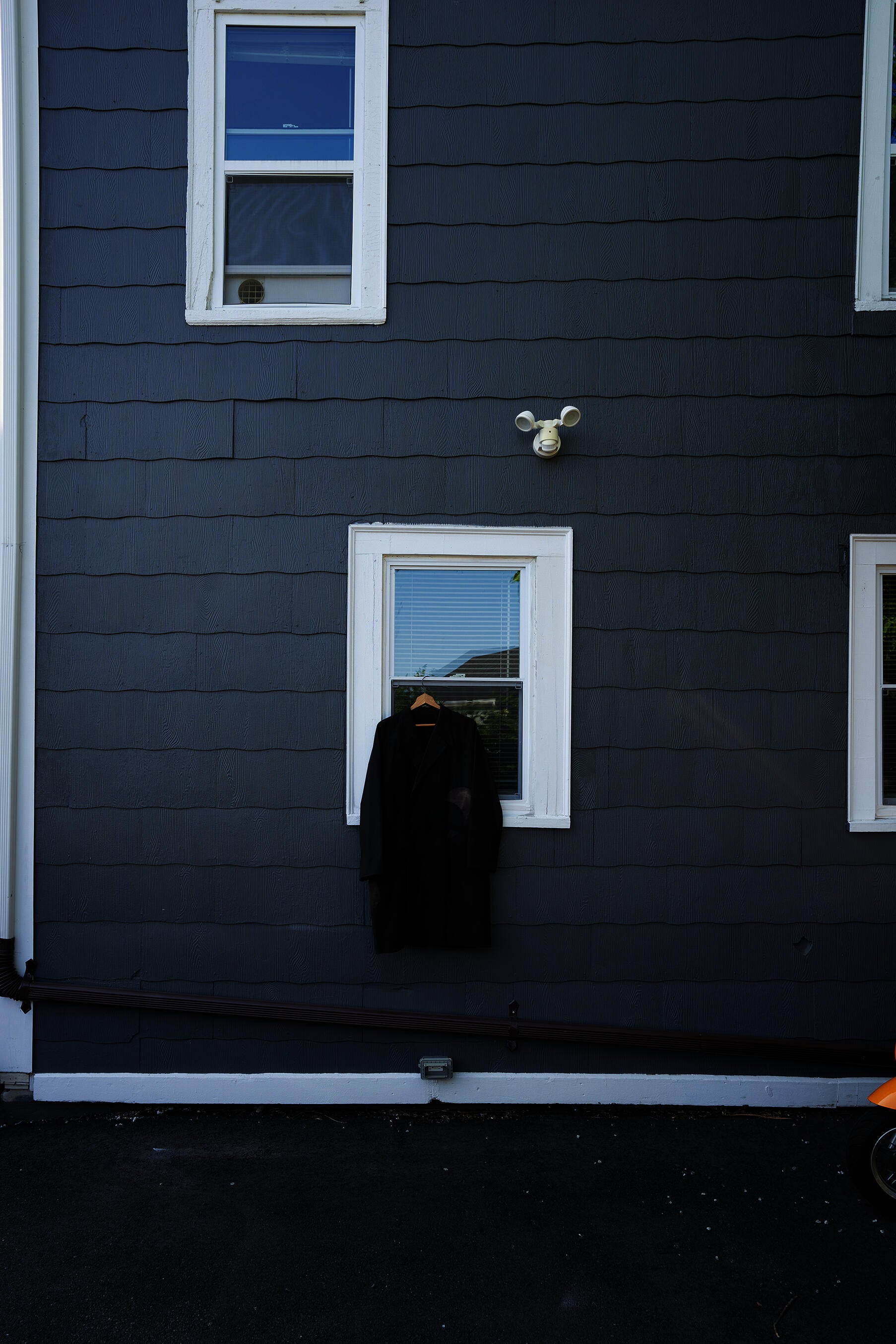 black coat hanging from a window on a grey house