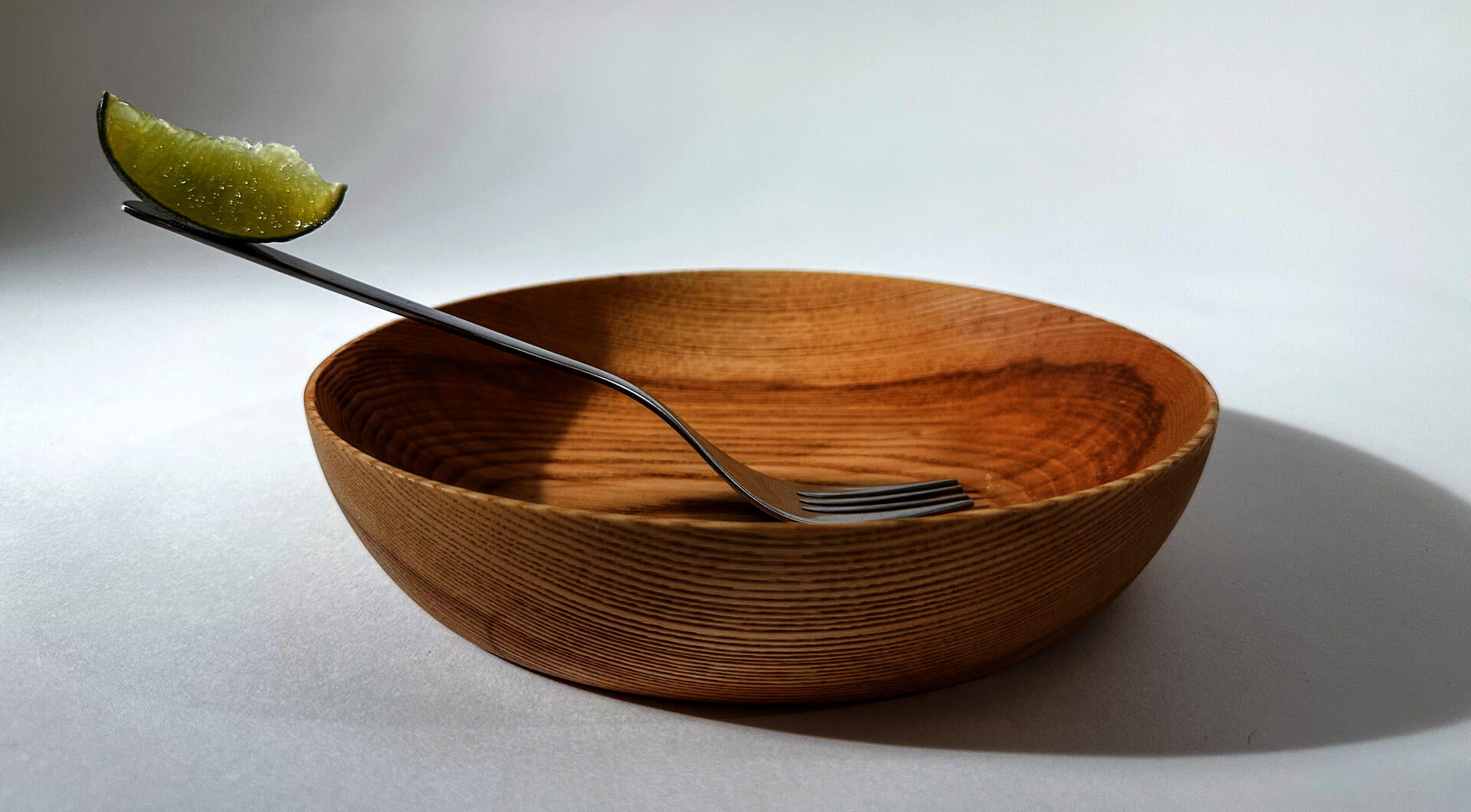A wooden bowl with a fork magnetically attached to the interior, with a slice of lime balancing on the end of the handle to demonstrate the magnetic pull.
